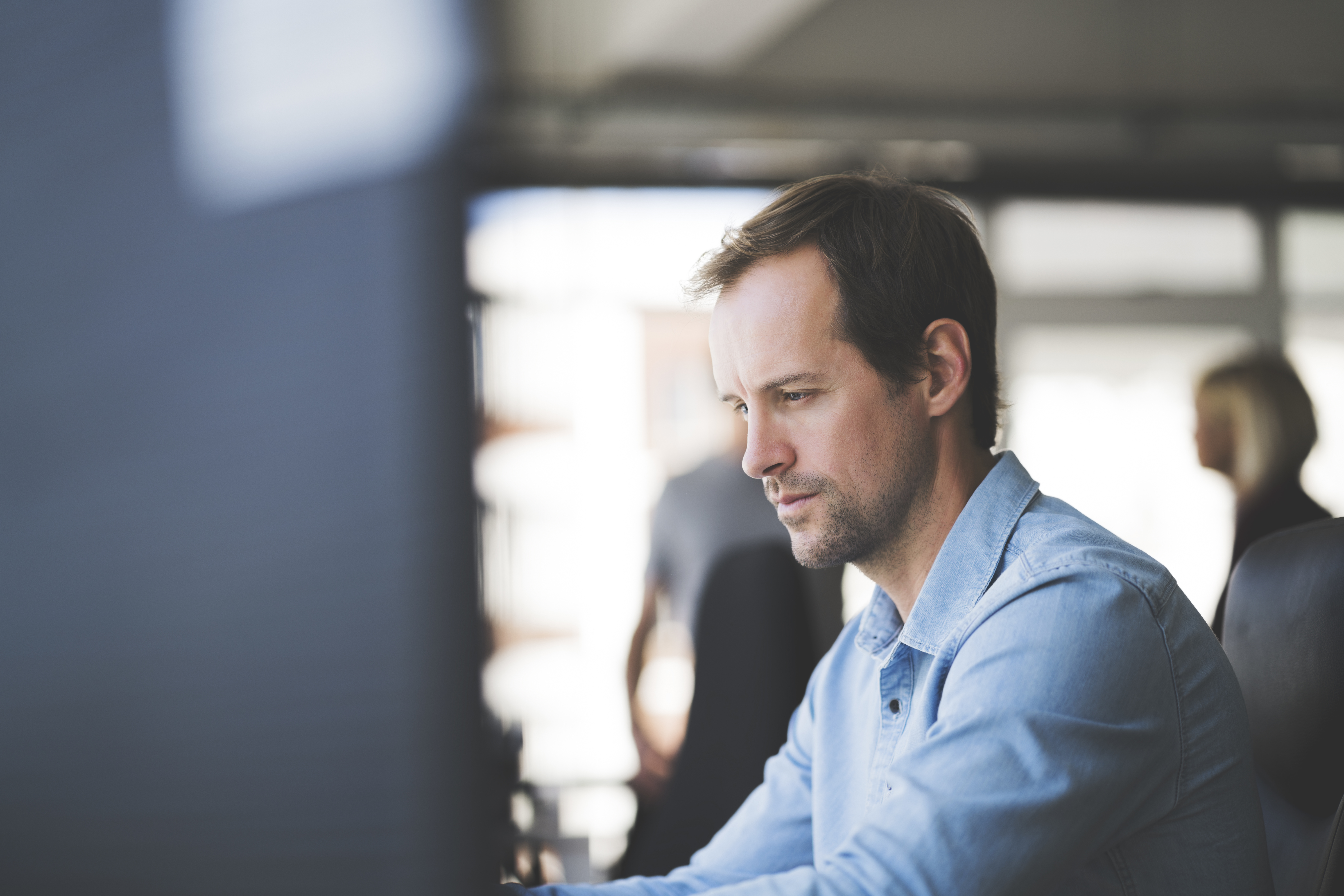 Man in a denim shirt focused on commercial real estate tax management consulting at his desk.