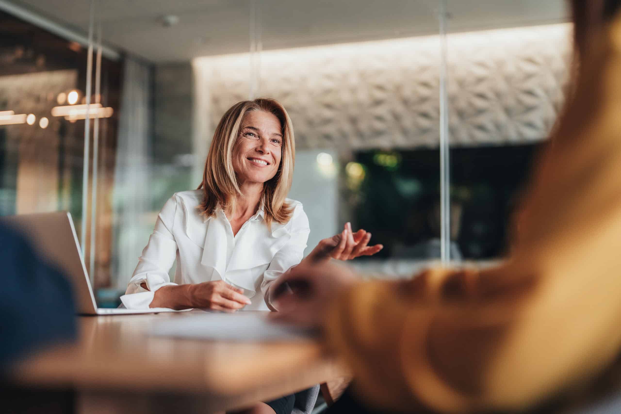 Smiling woman in white blouse discusses commercial real estate tech strategy at a modern office table.