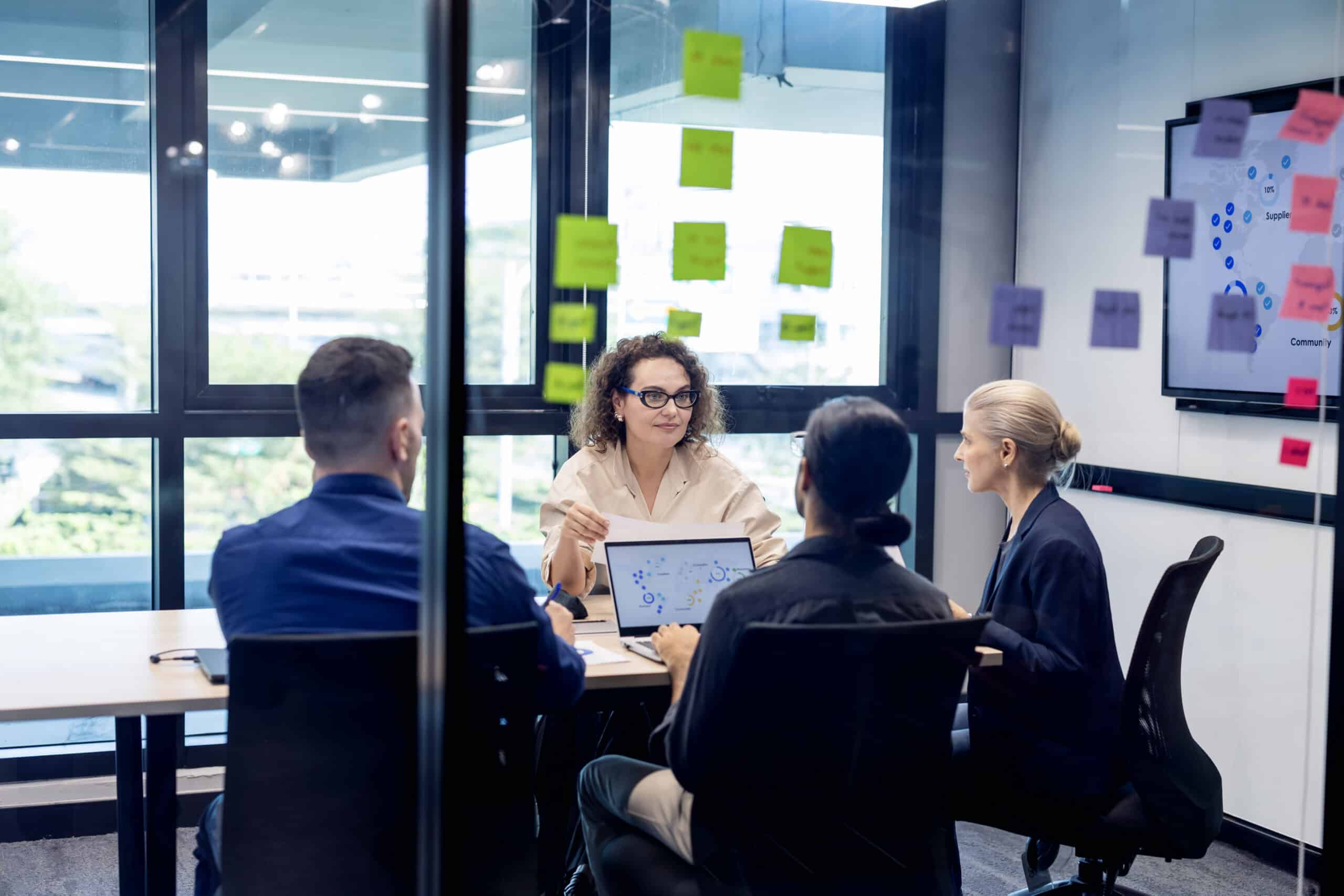 Four people discuss a document in a meeting room, planning commercial real estate tech strategy.