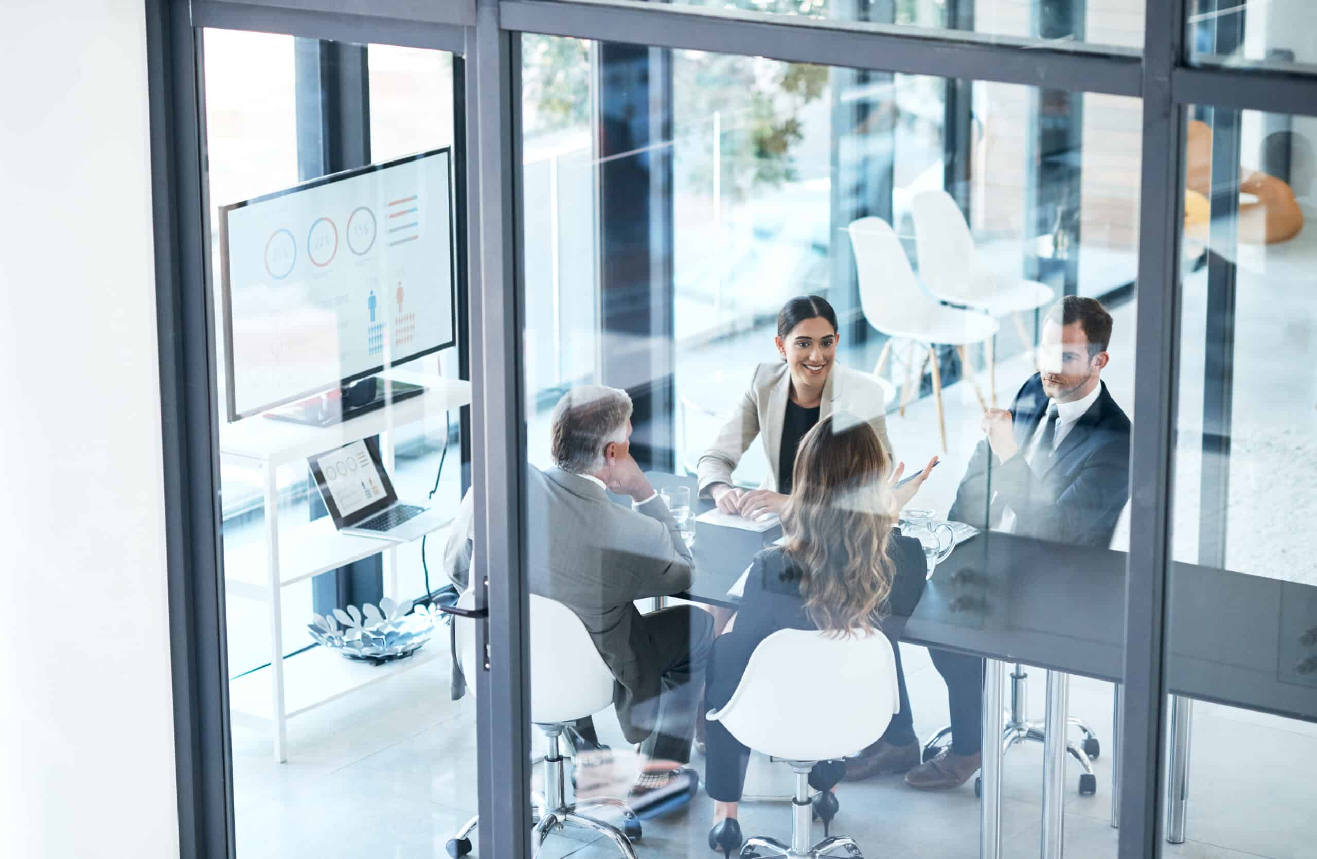 Four people in business attire discuss data quality services in a glass-walled office.