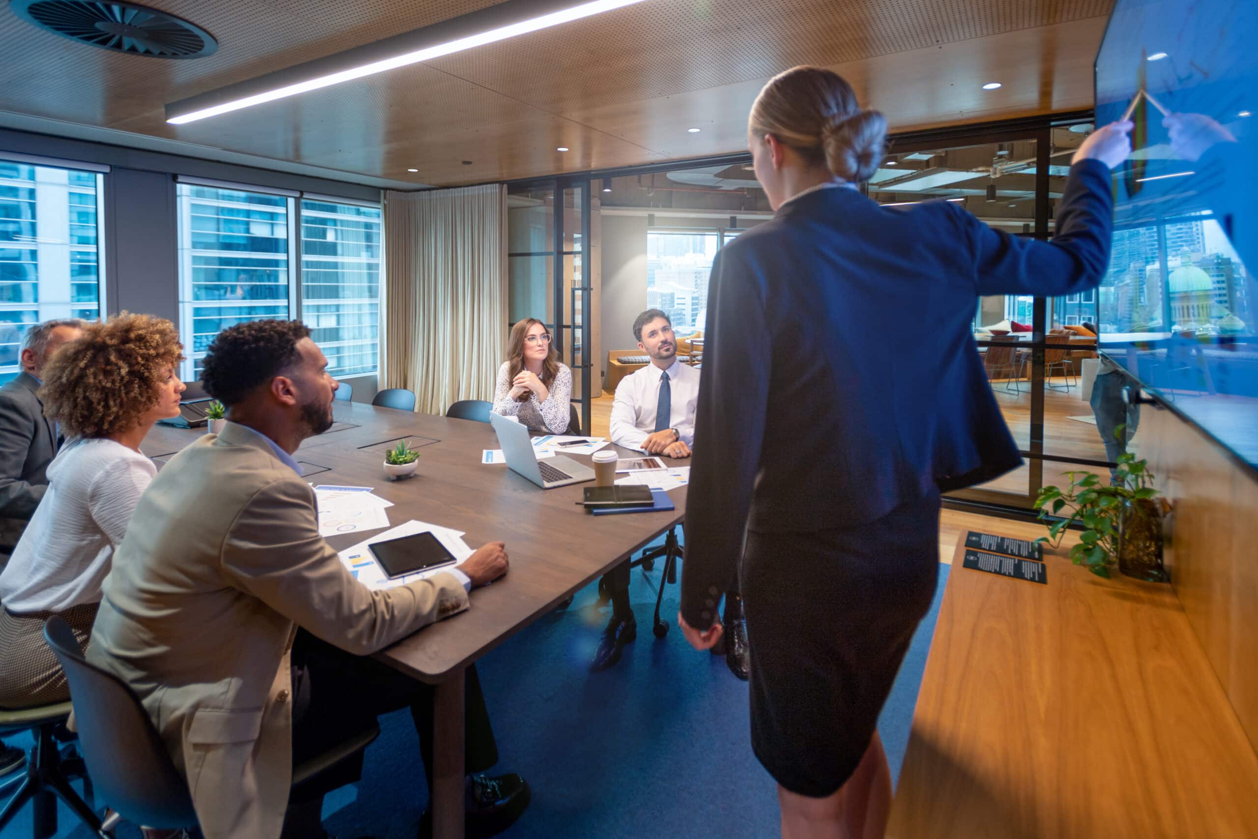 Businesswoman presenting a demand forecasting graph to colleagues in a modern conference room.