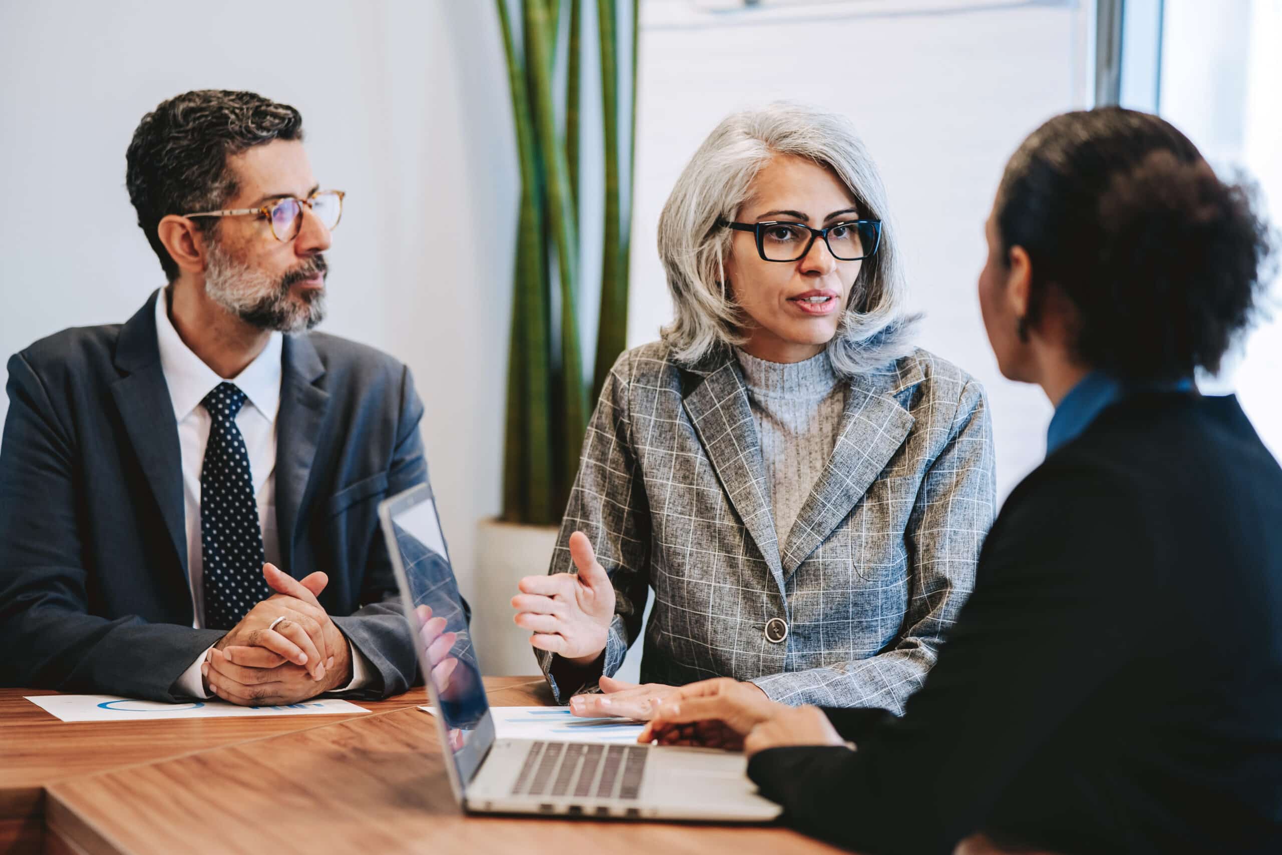 Three business professionals discuss digital twins consulting at a table with a laptop and documents.