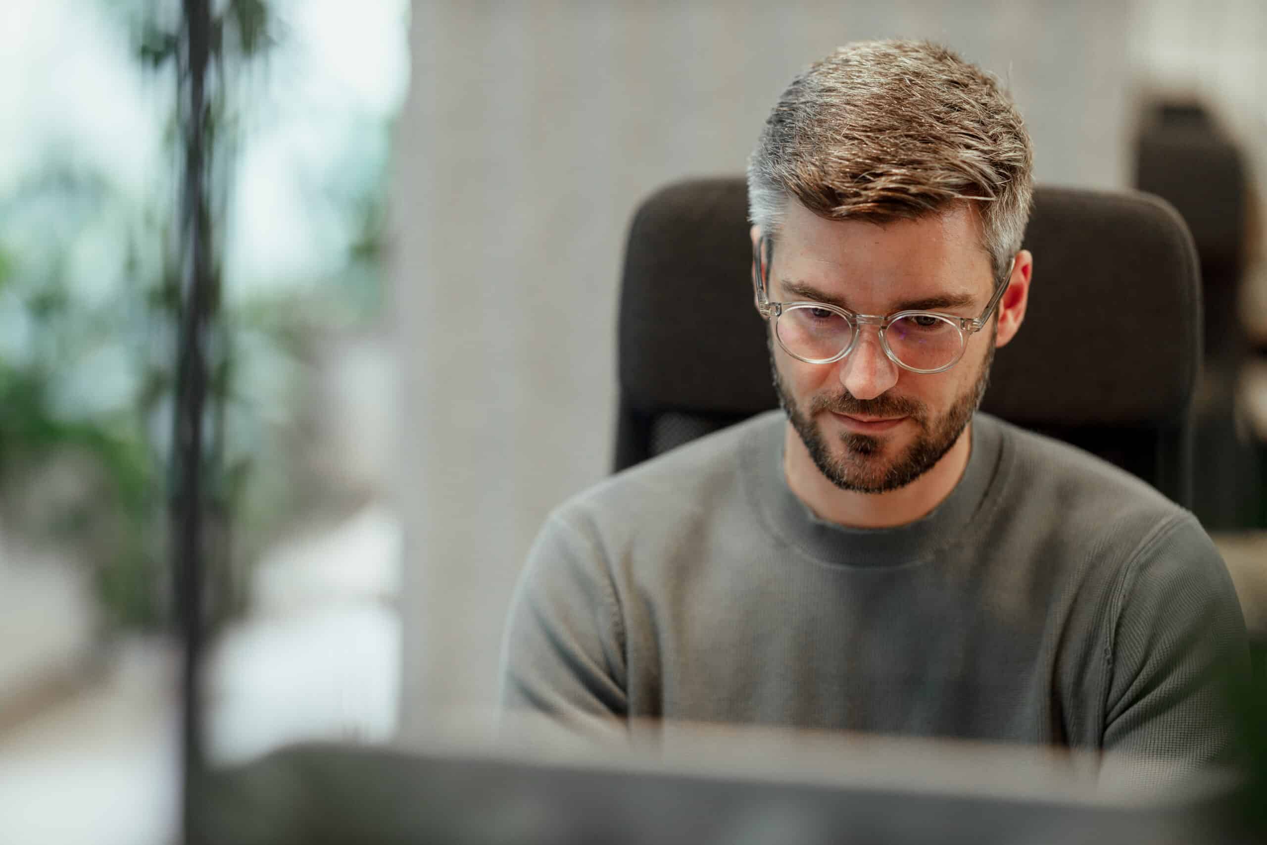 Man with glasses and beard working on digital twins consulting in an office setting.