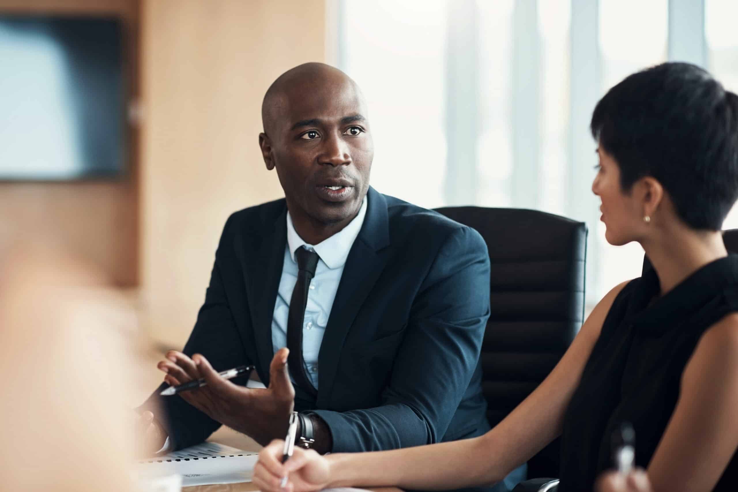 Businessman in a suit discussing eminent domain consulting with a colleague in an office meeting.