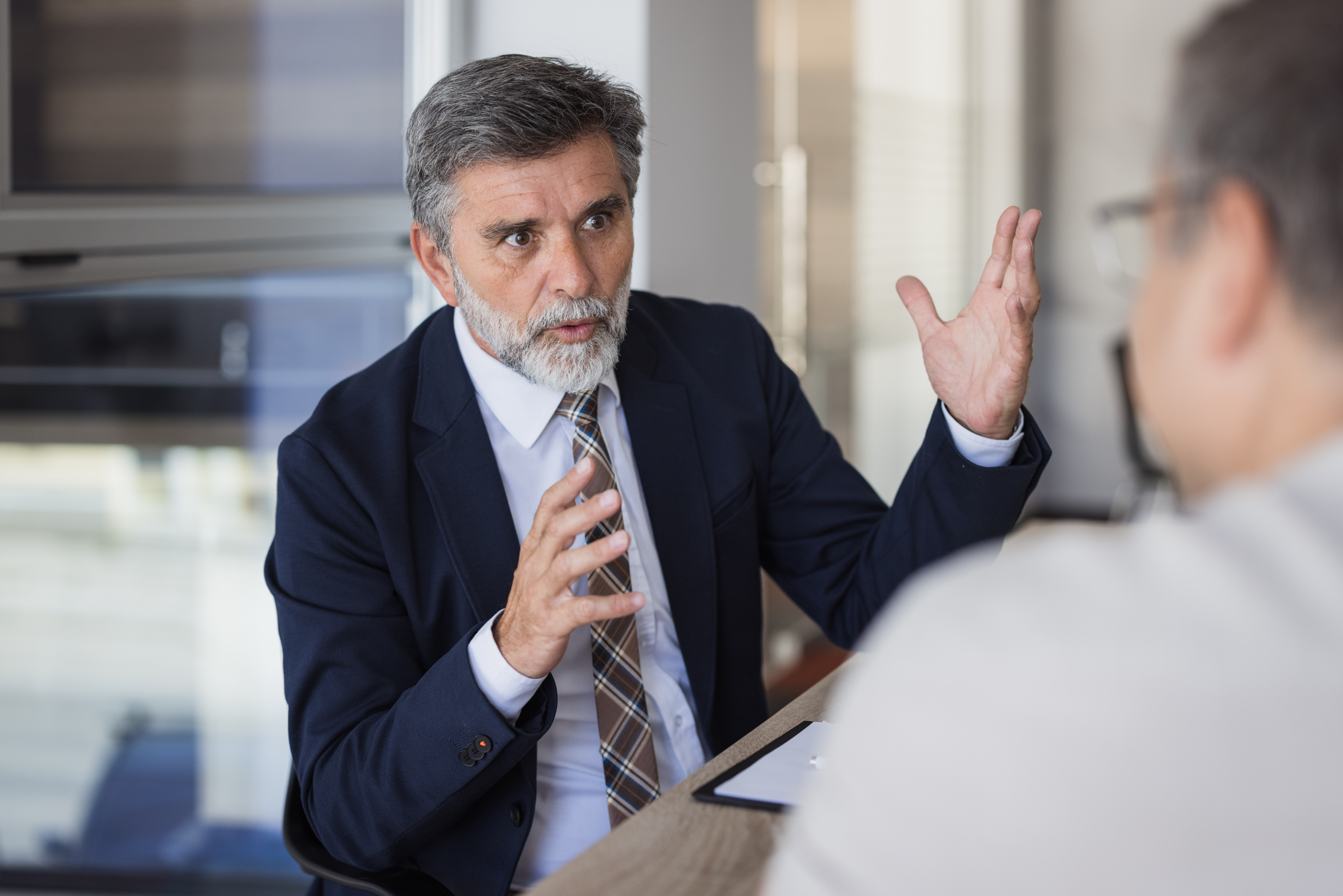Older man in suit discusses eminent domain consulting with a colleague in an office setting.