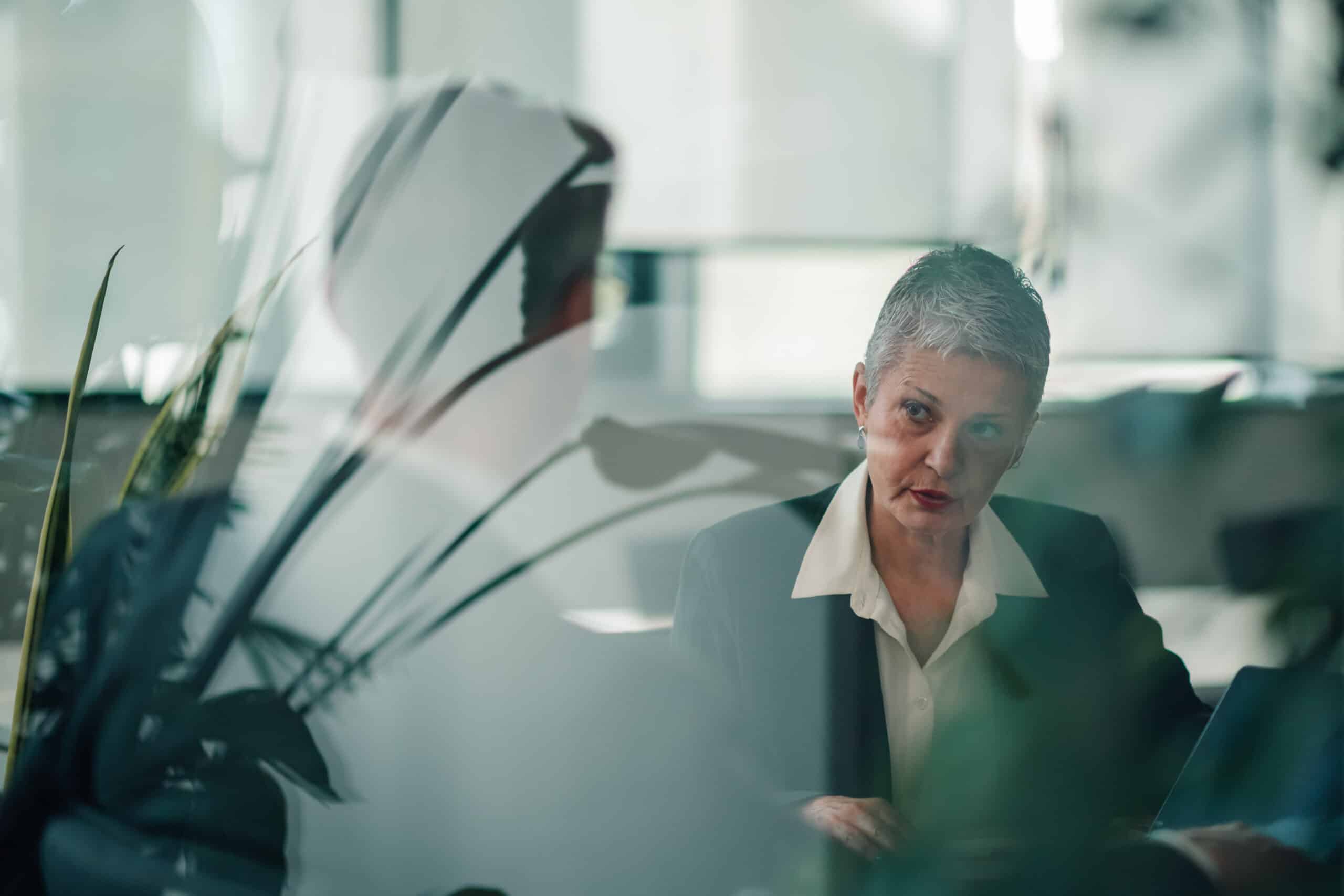 Two eminent domain consultants have a serious discussion in an office, seen through glass.