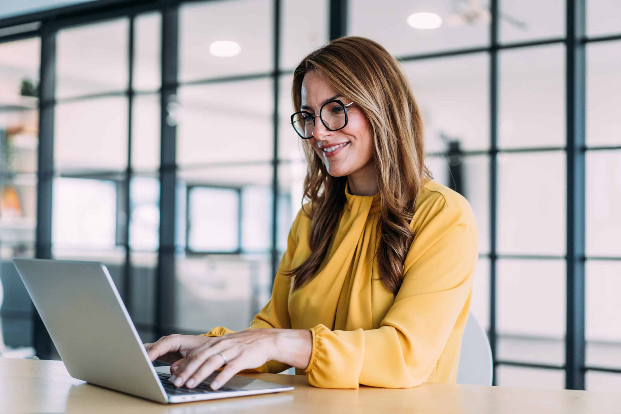 Woman with glasses in a yellow blouse smiles while working on enterprise application integration.