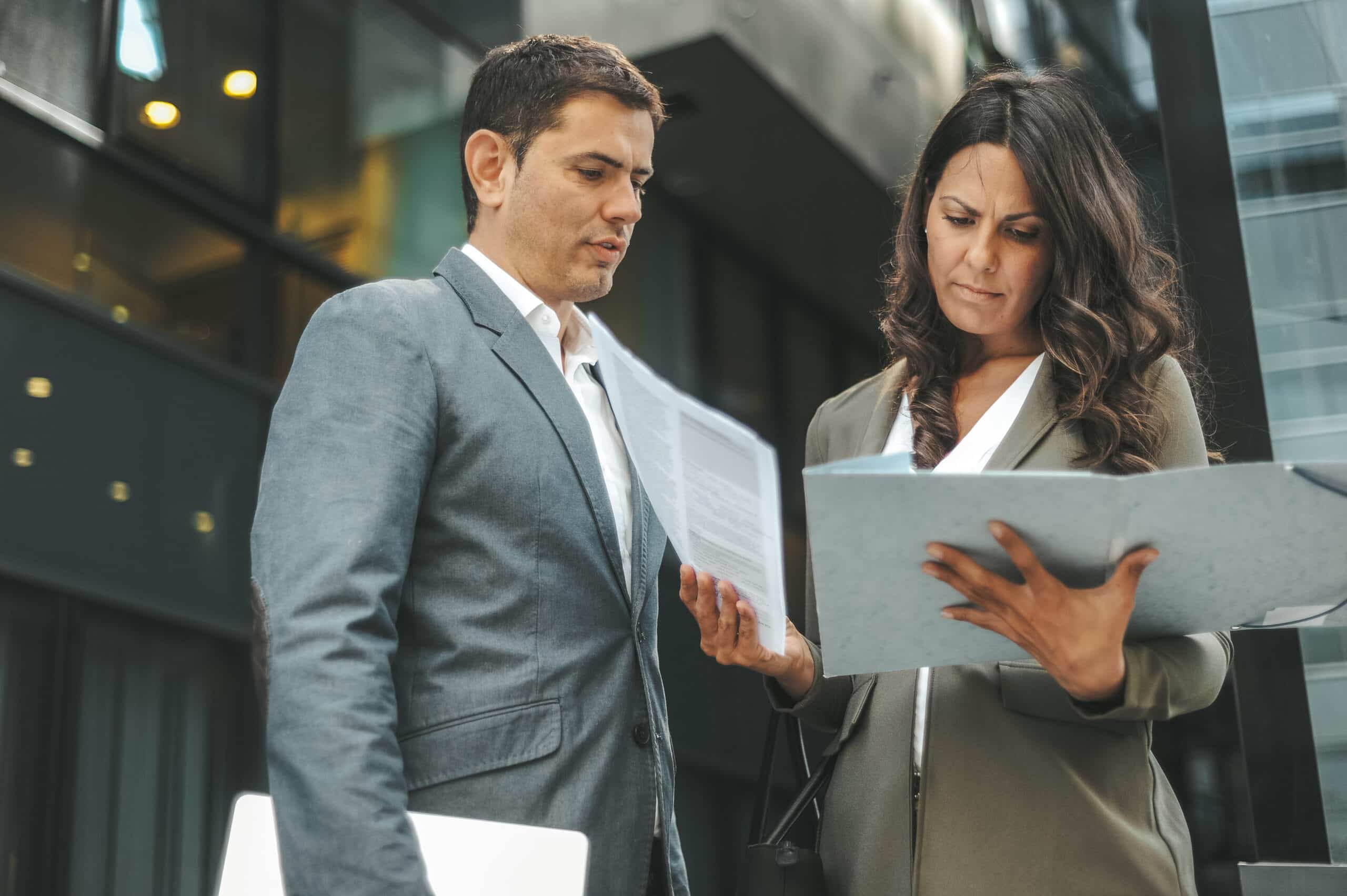 Two business professionals discuss expert witness services outside an office building.