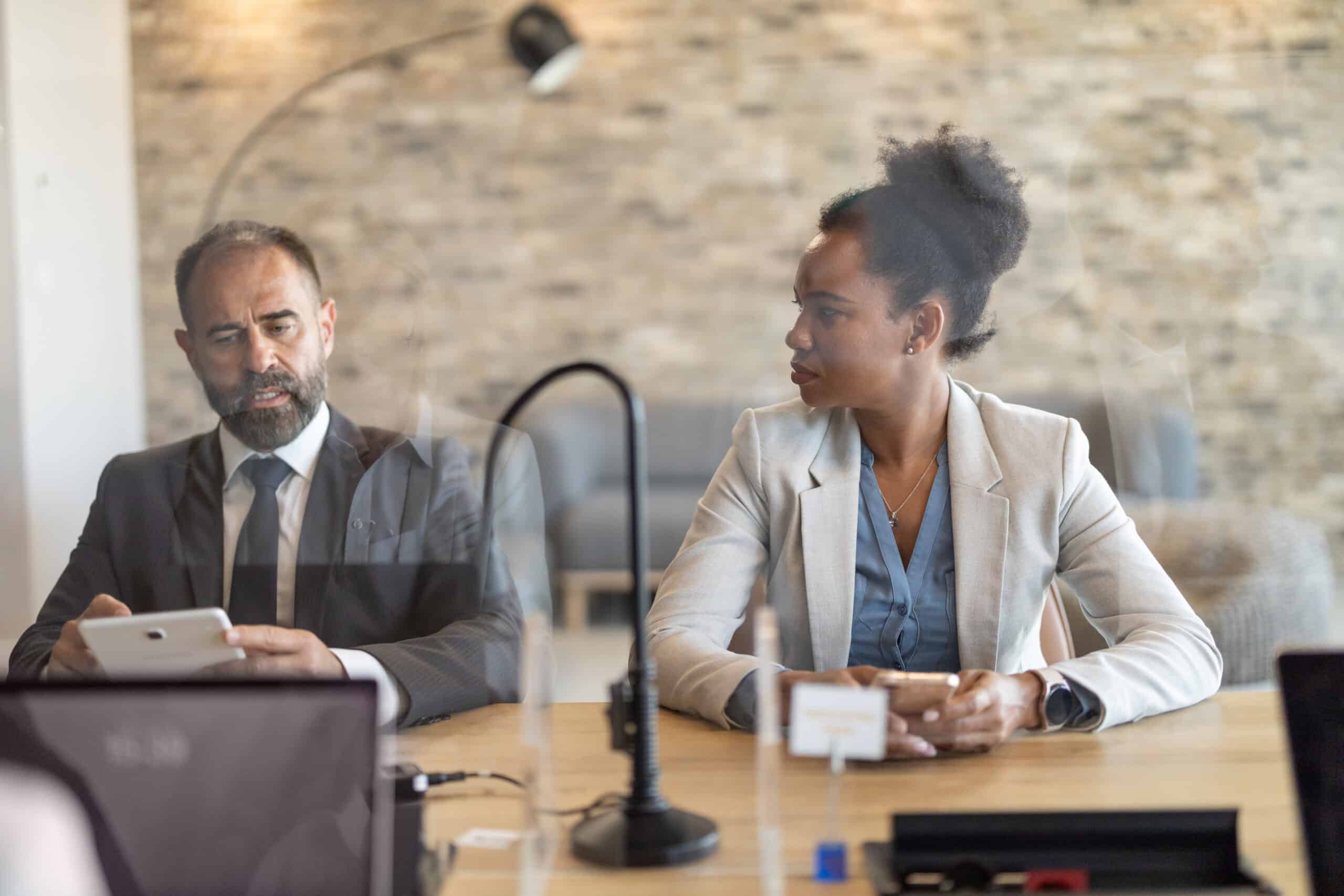 Two businesspeople discuss expert witness services with laptops and coffee at their table.