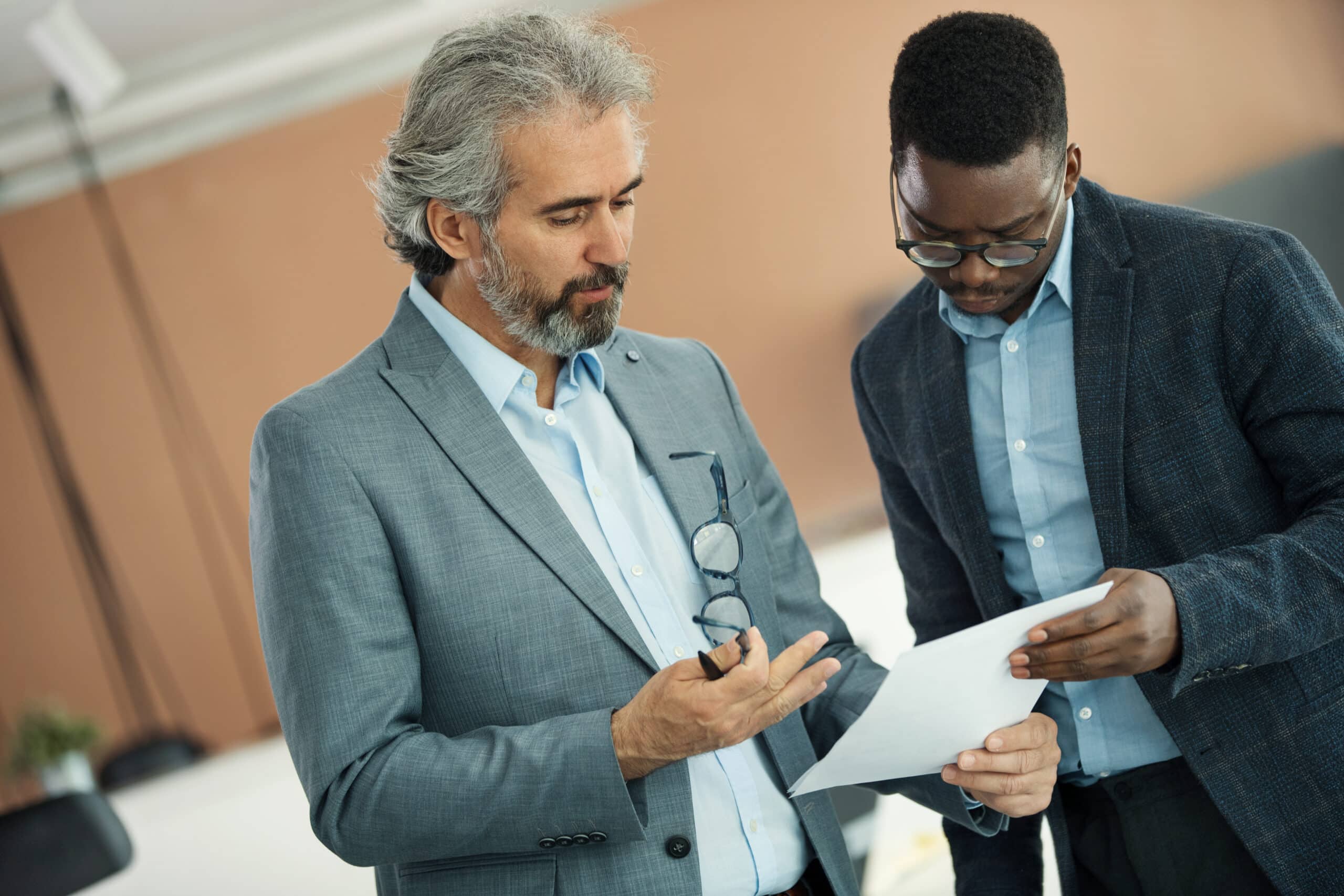 Two men in suits discuss a document on IT architecture consulting in an office setting.