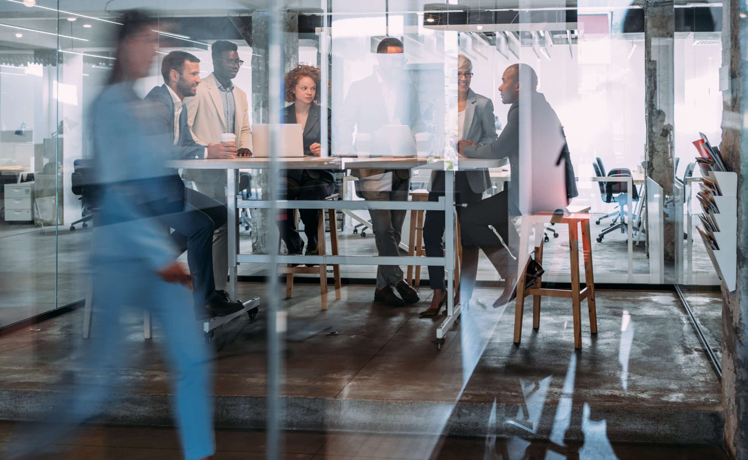Business team discusses IT governance in a glass-walled office as one person walks by.