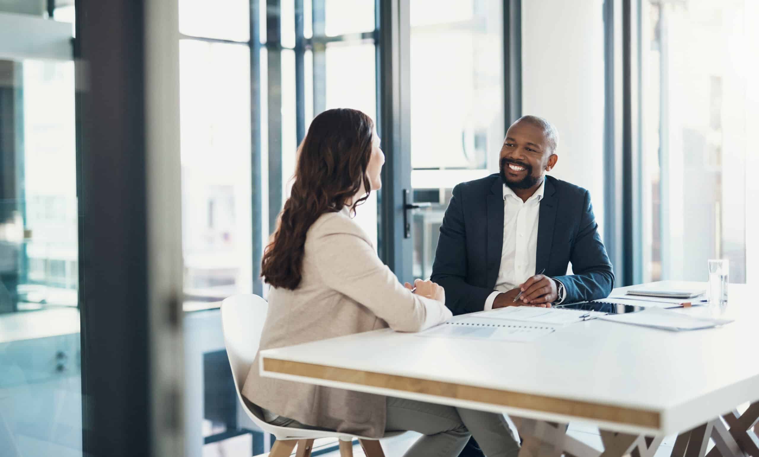 Two people discussing IT infrastructure consulting at a bright office table, both smiling.