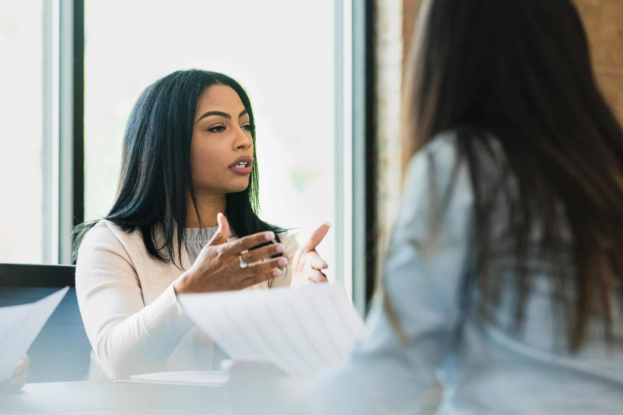Two women discuss it infrastructure consulting across a table, engaged in a serious conversation.