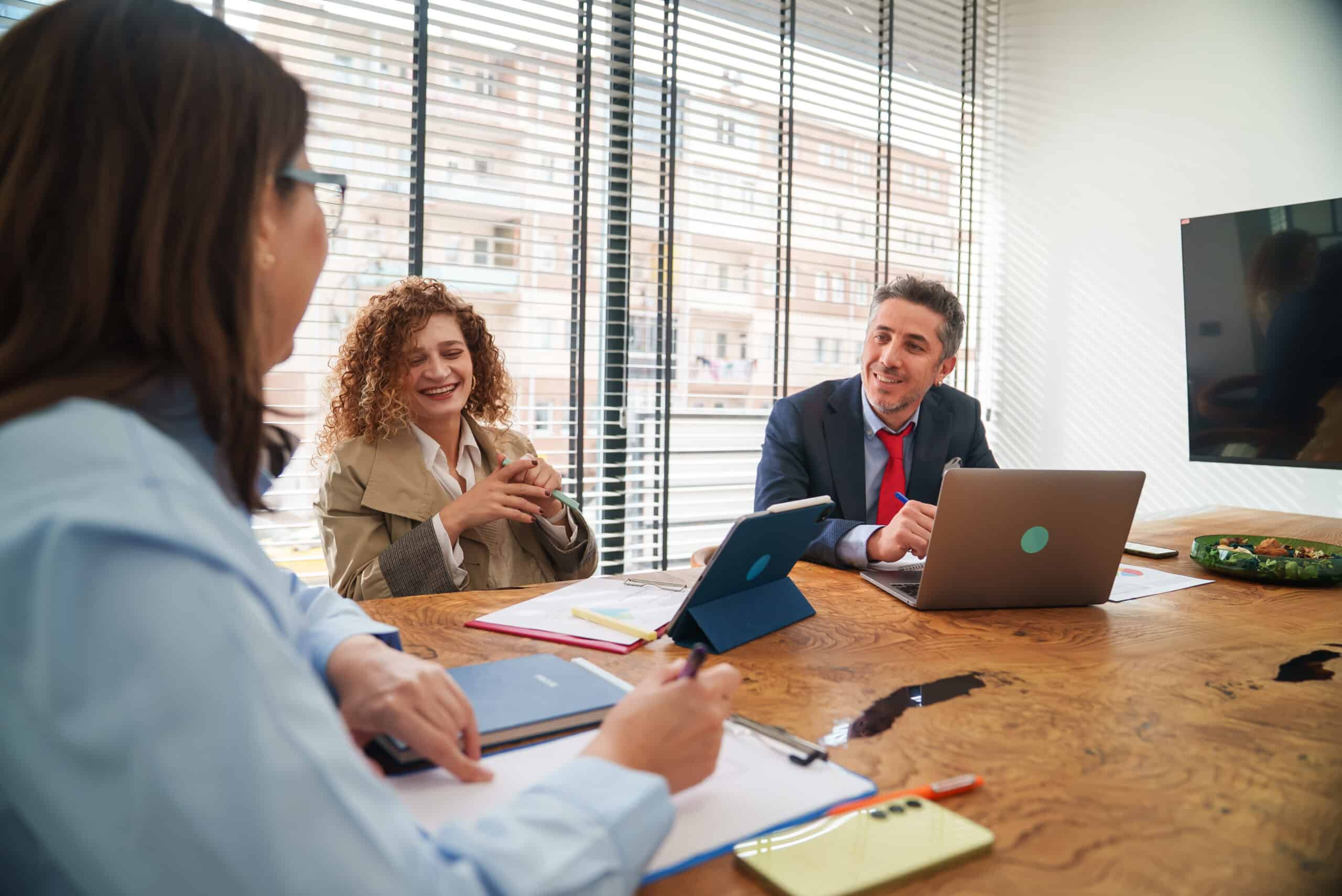 Three it modernization consultants meet in business attire around a table with laptops and documents.
