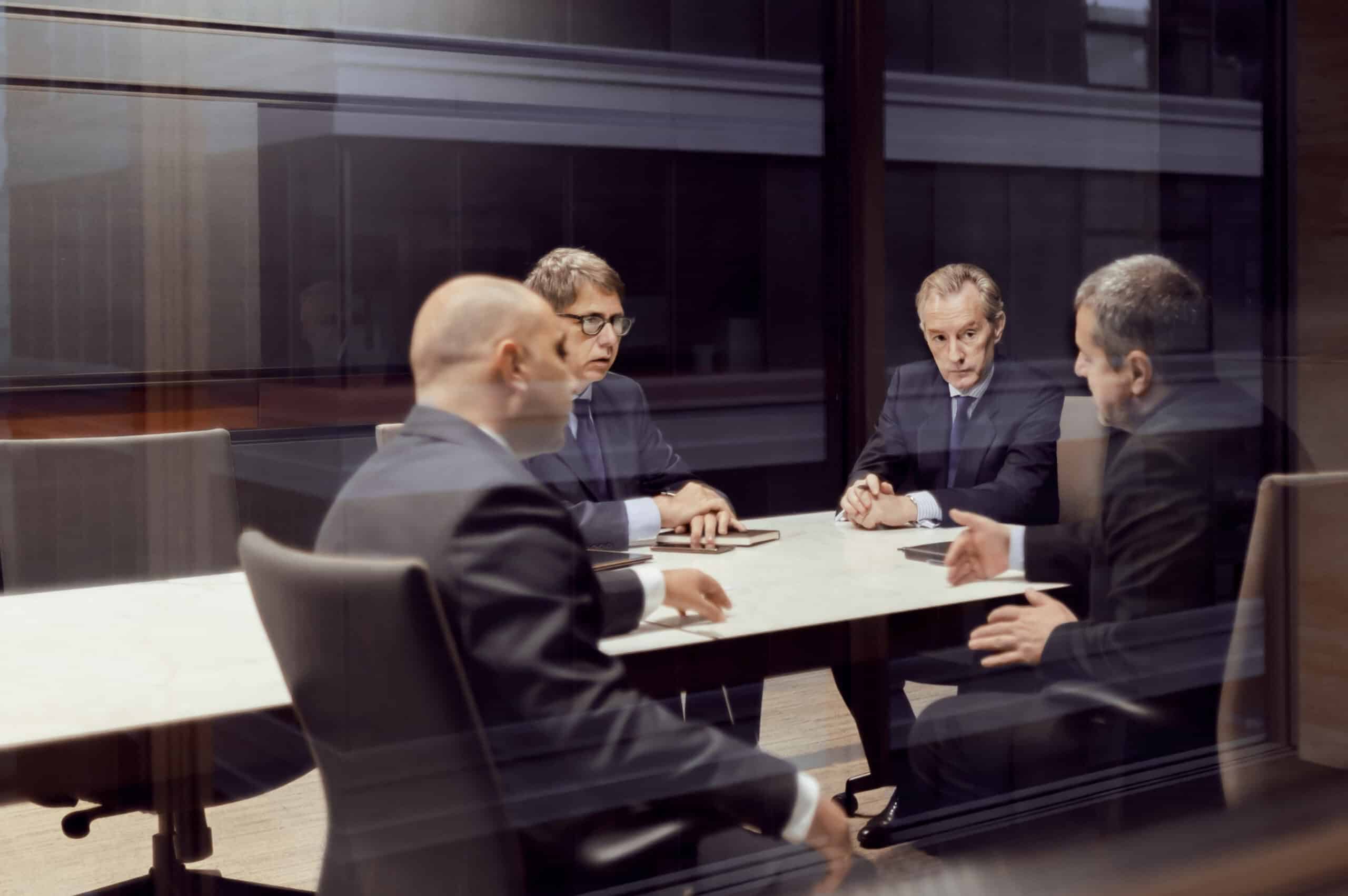 Four men in business suits discuss IT modernization around a conference table in an office.