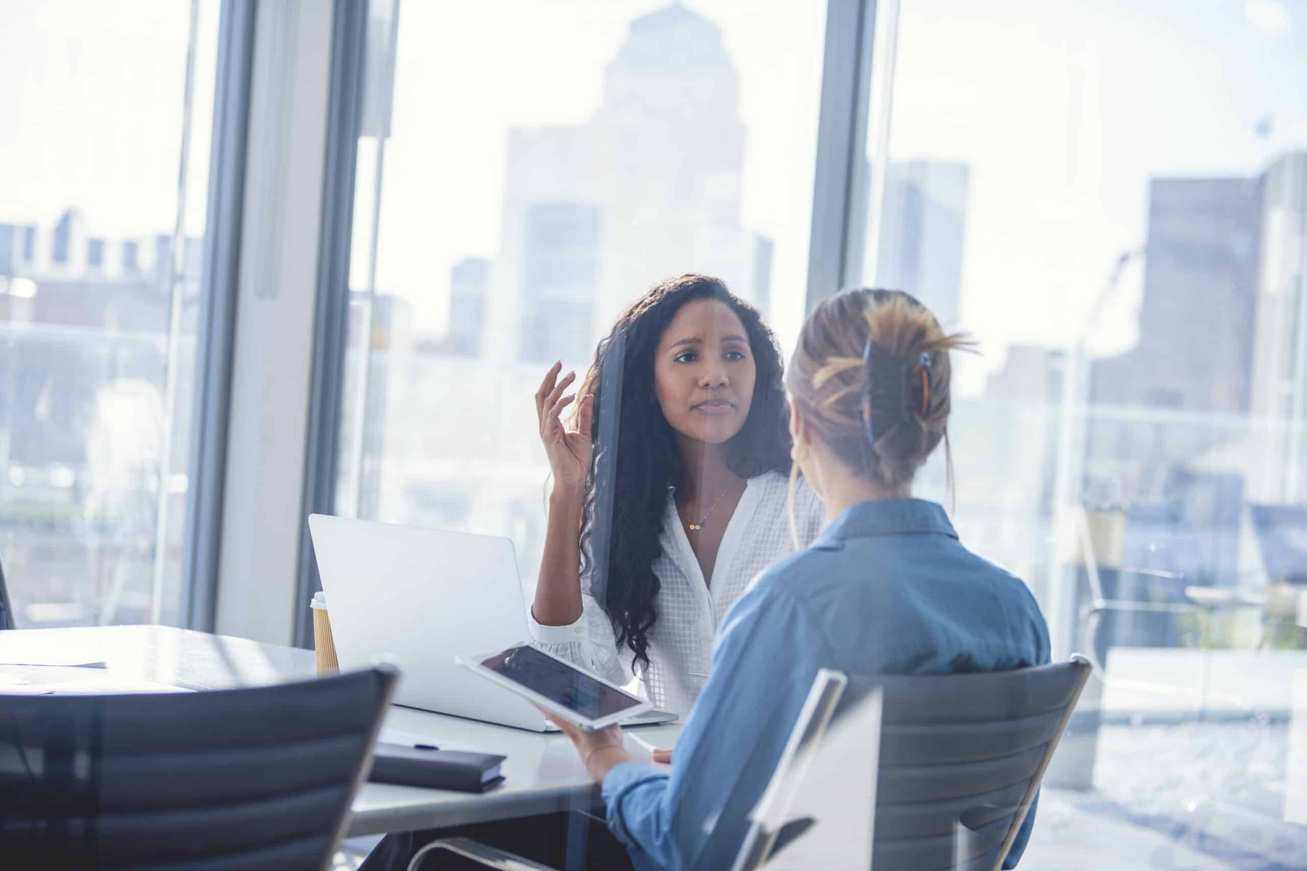 Two women discuss intelligent automation at a modern office table with laptops and a tablet.