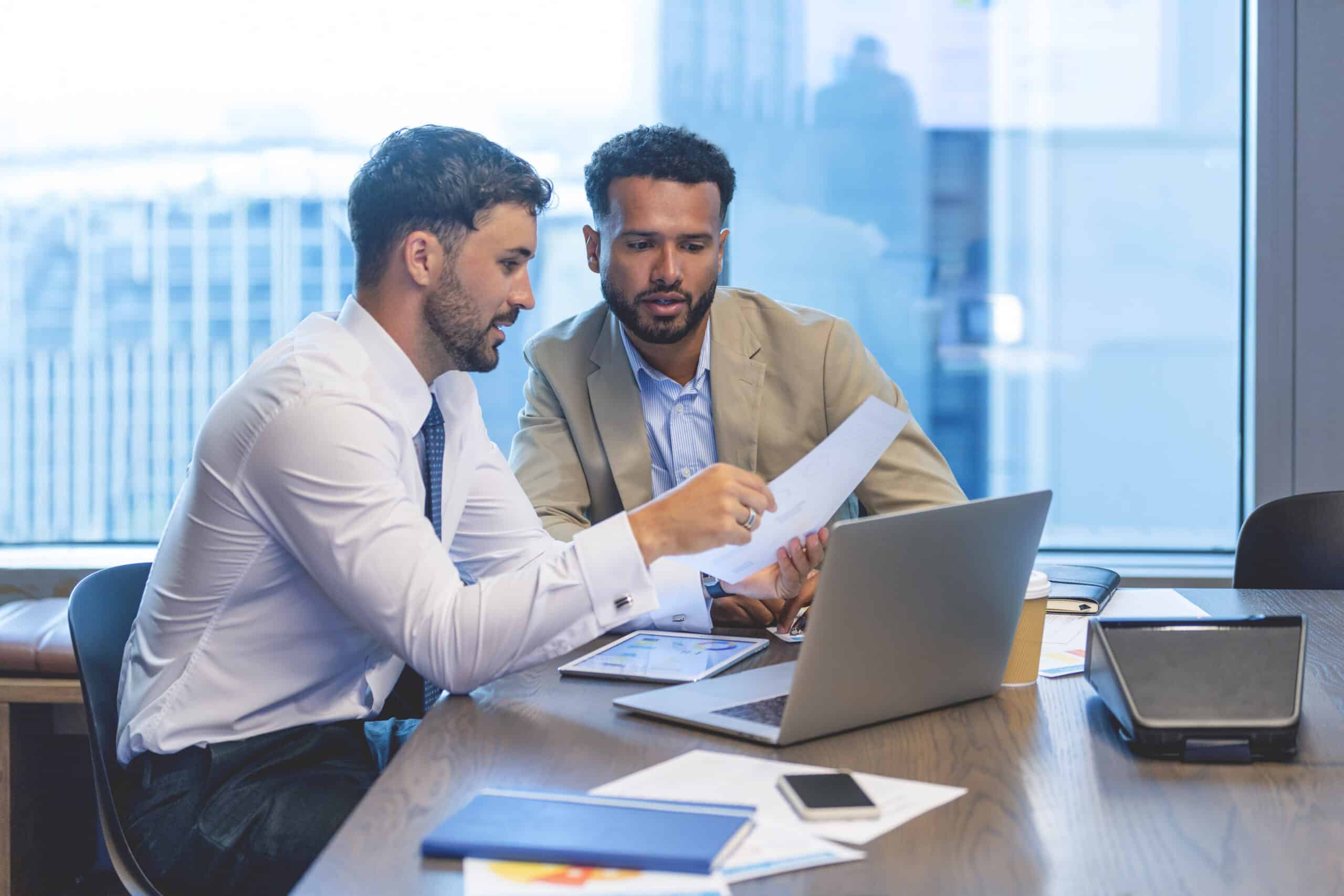 Two businessmen discuss documents and intelligent automation at a laptop in a modern office.