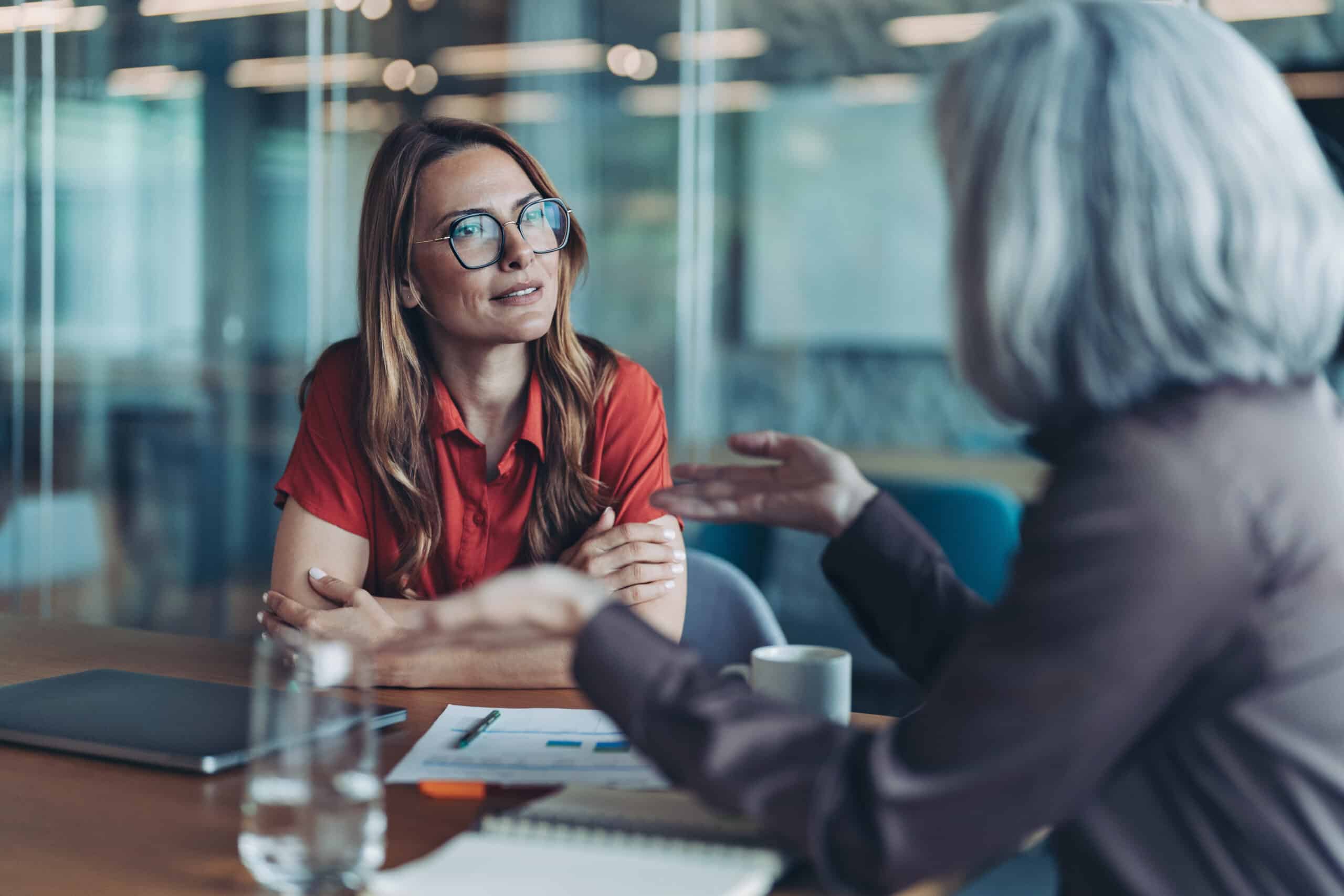 Two women discuss intelligent automation consulting at a table in a modern office setting.