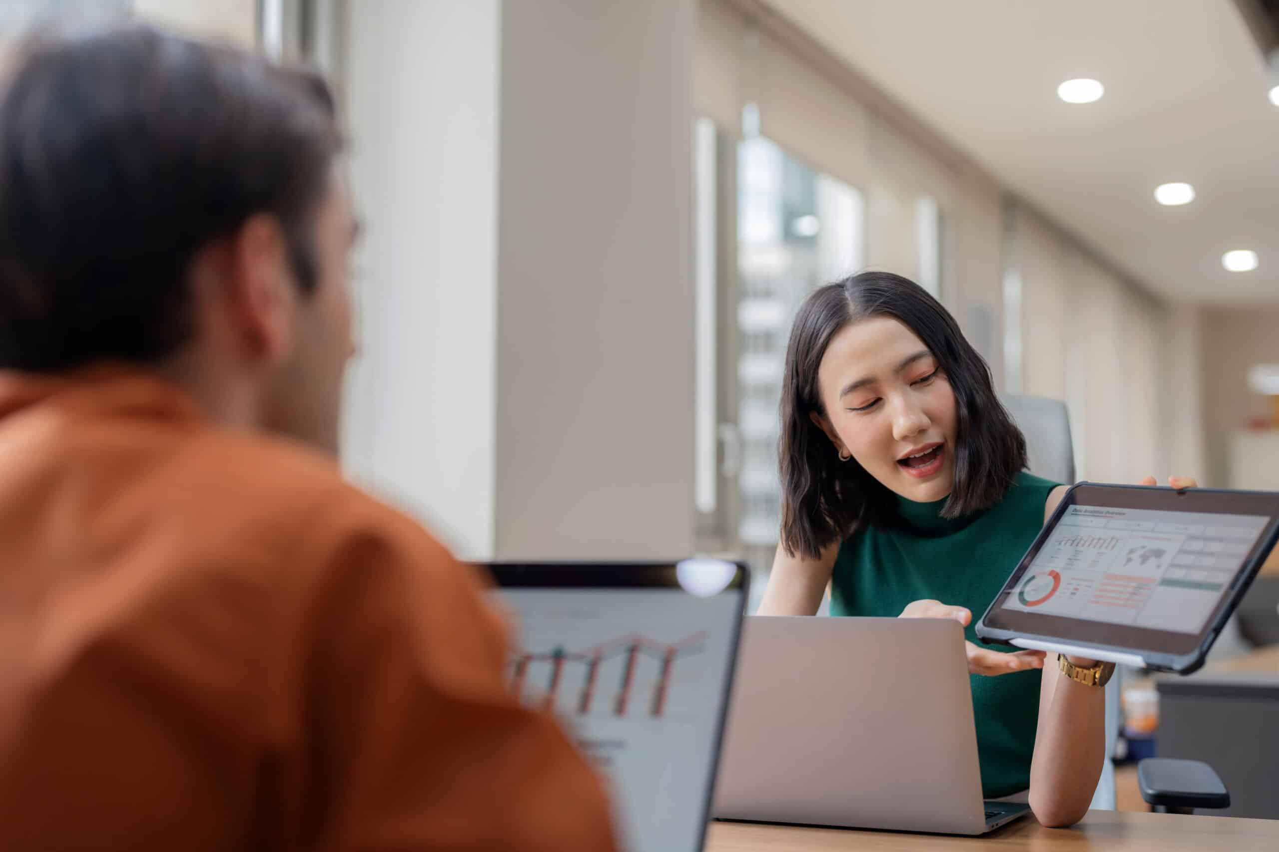 Woman showing IoT Consulting charts on a tablet to a colleague during an office meeting.