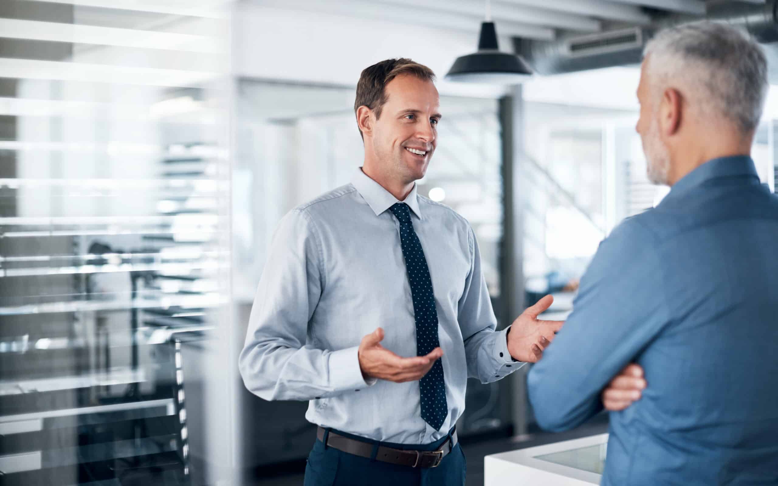 Two men in business attire discuss land use planning consulting in a modern office setting.