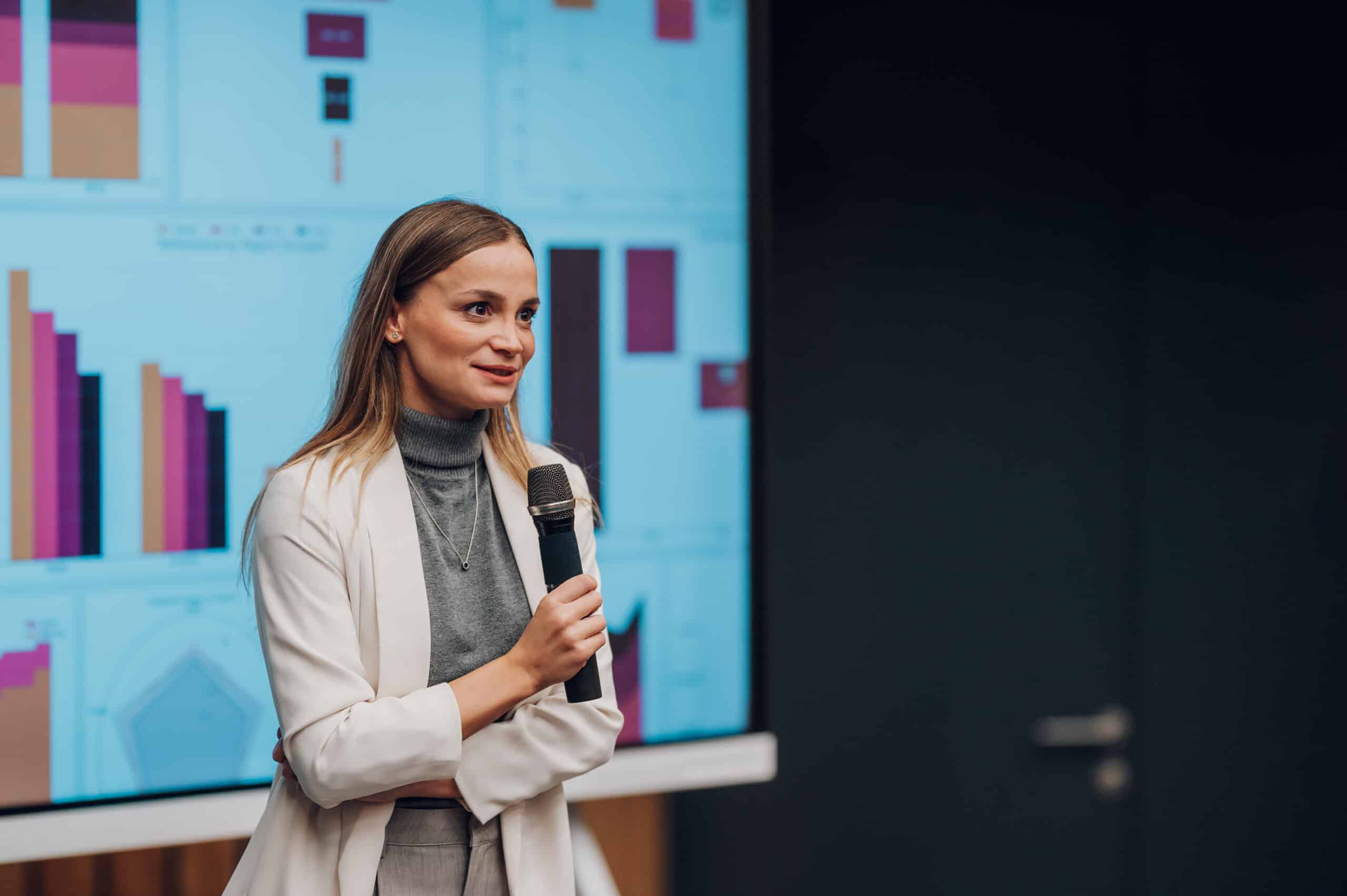 Woman in a blazer discusses land use planning consulting before a screen of colorful graphs.
