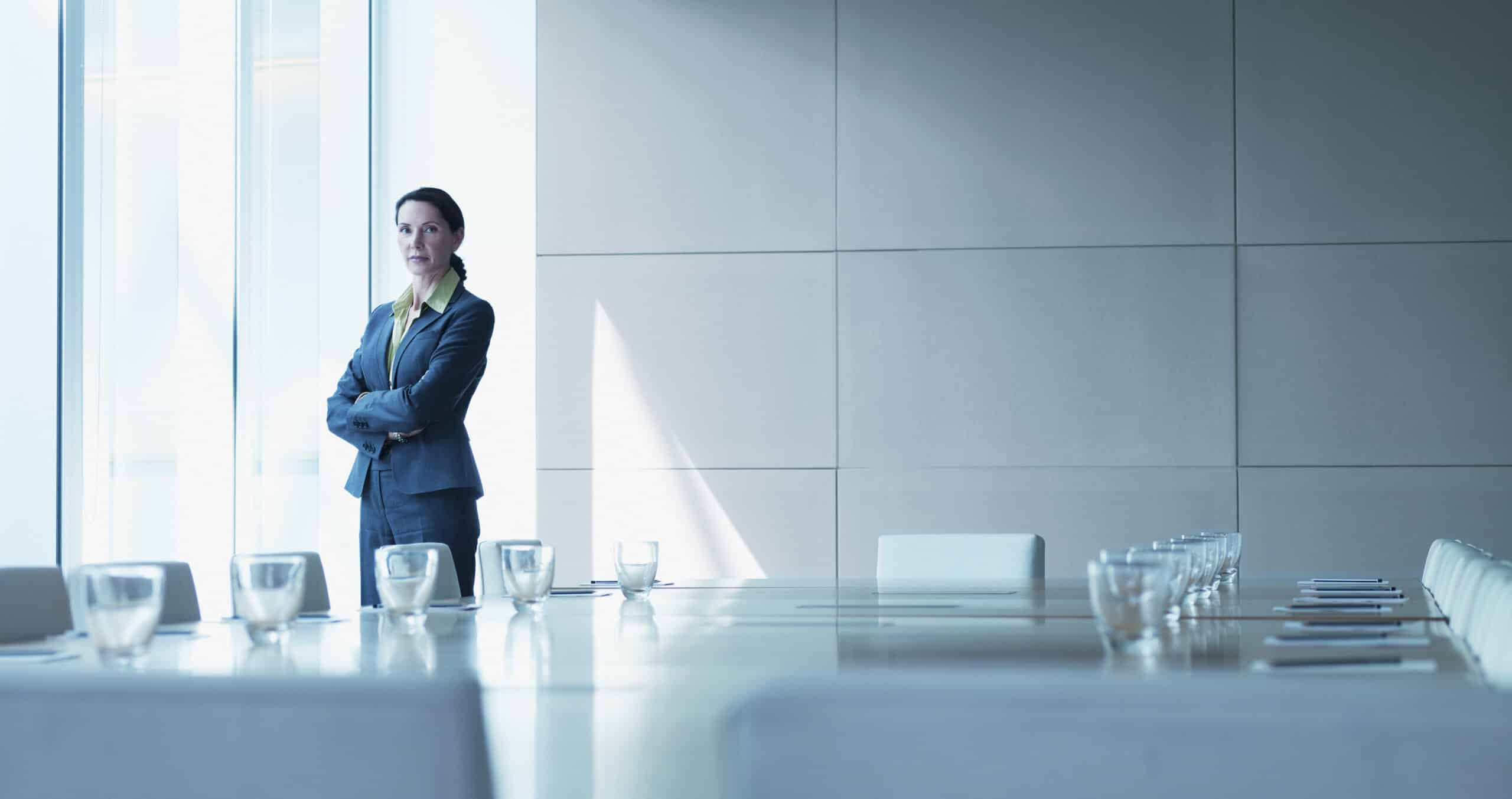 Woman in a suit, expert in land use planning consulting, stands by a window in modern conference room.