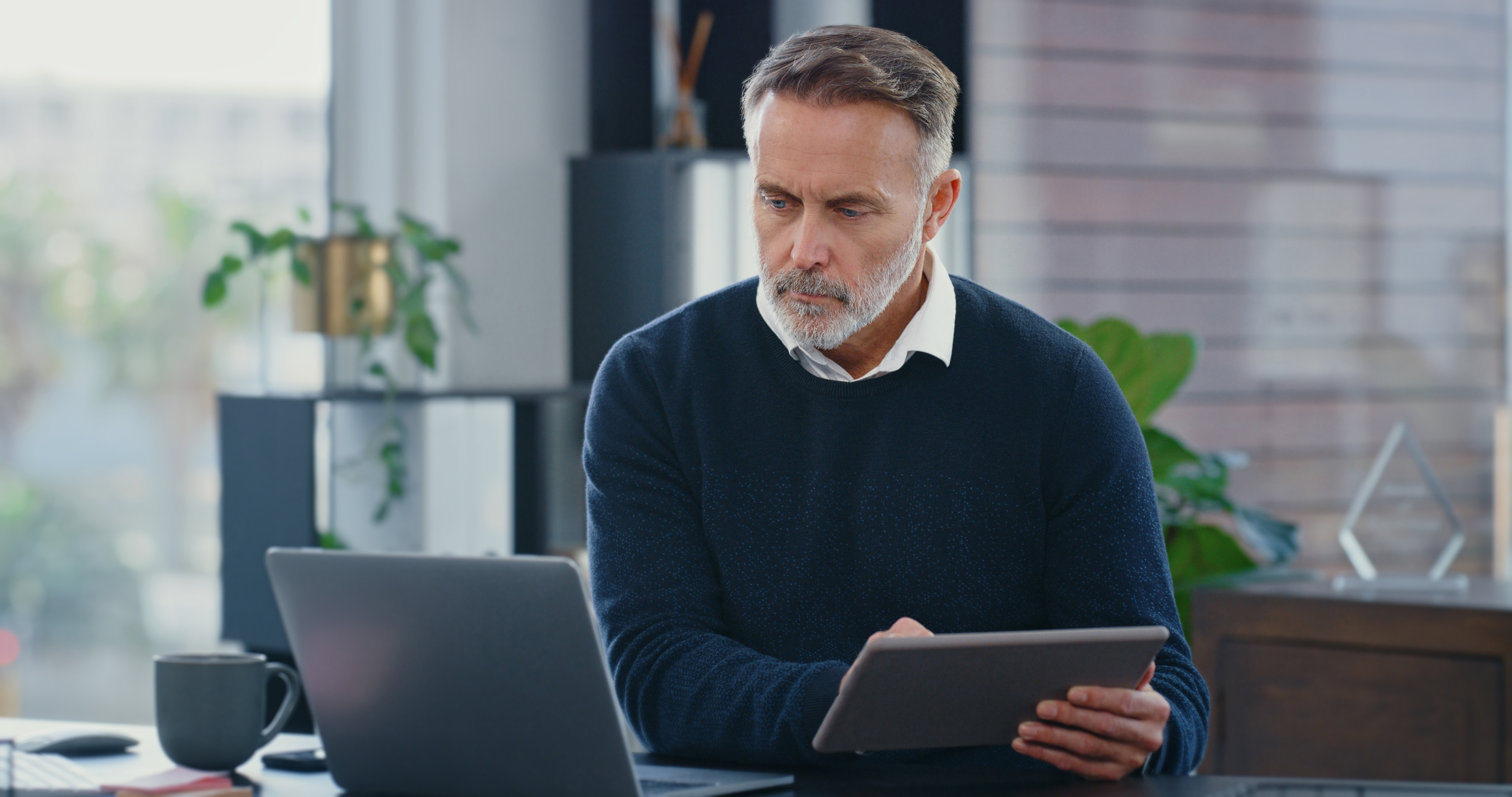 Man with gray hair using laptop and tablet at desk, working on land use planning consulting.