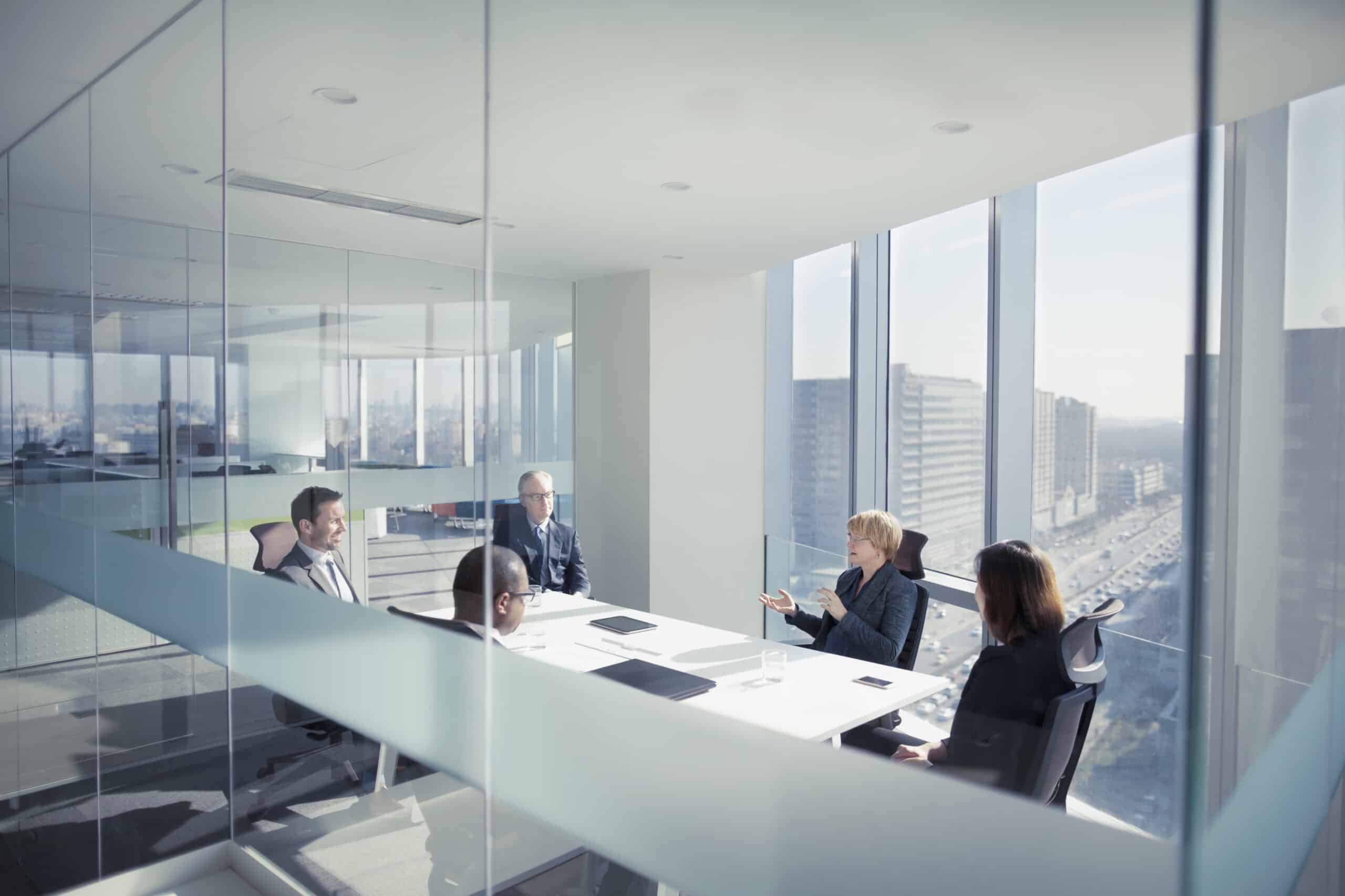 Five people in business attire discuss leadership development in a modern office with city views.
