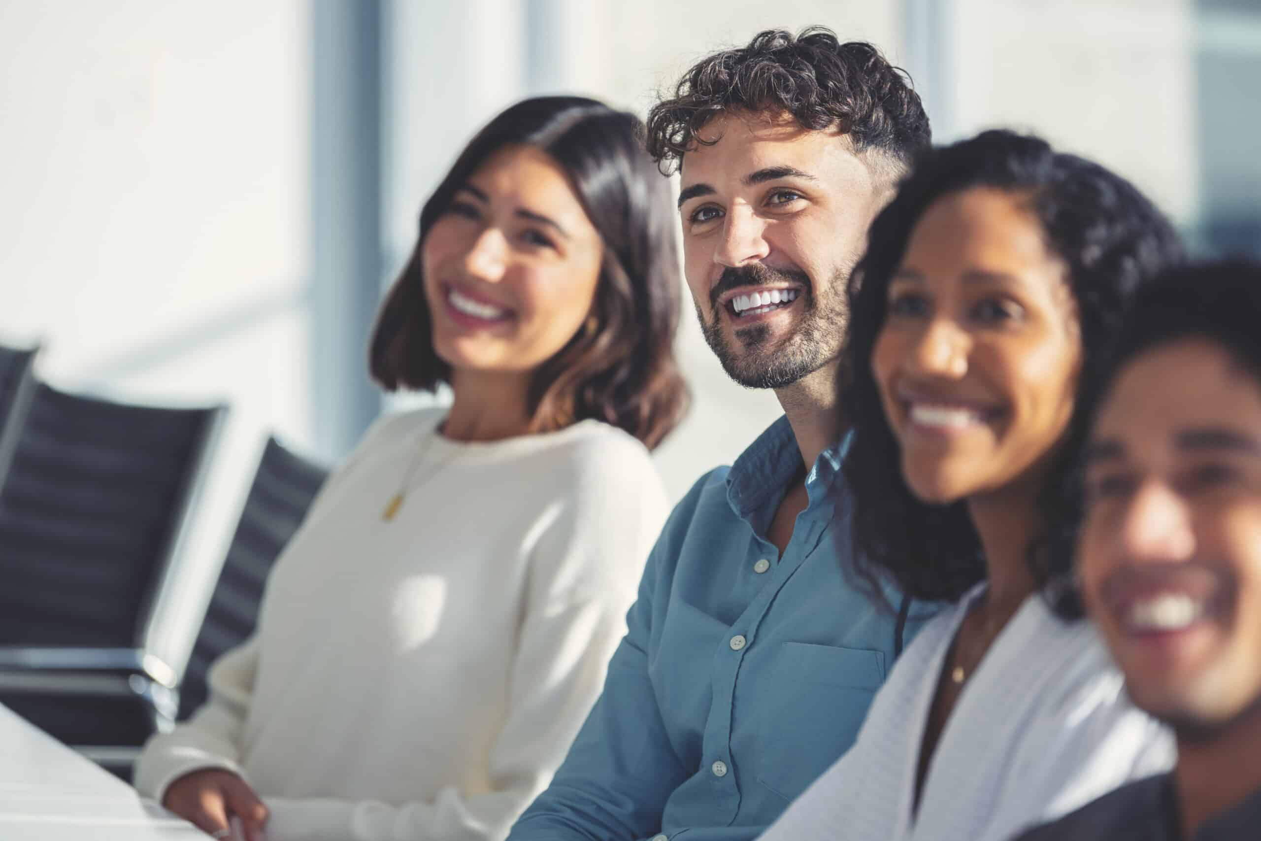 Four leadership development consultants sit in a row, smiling in a bright office setting.