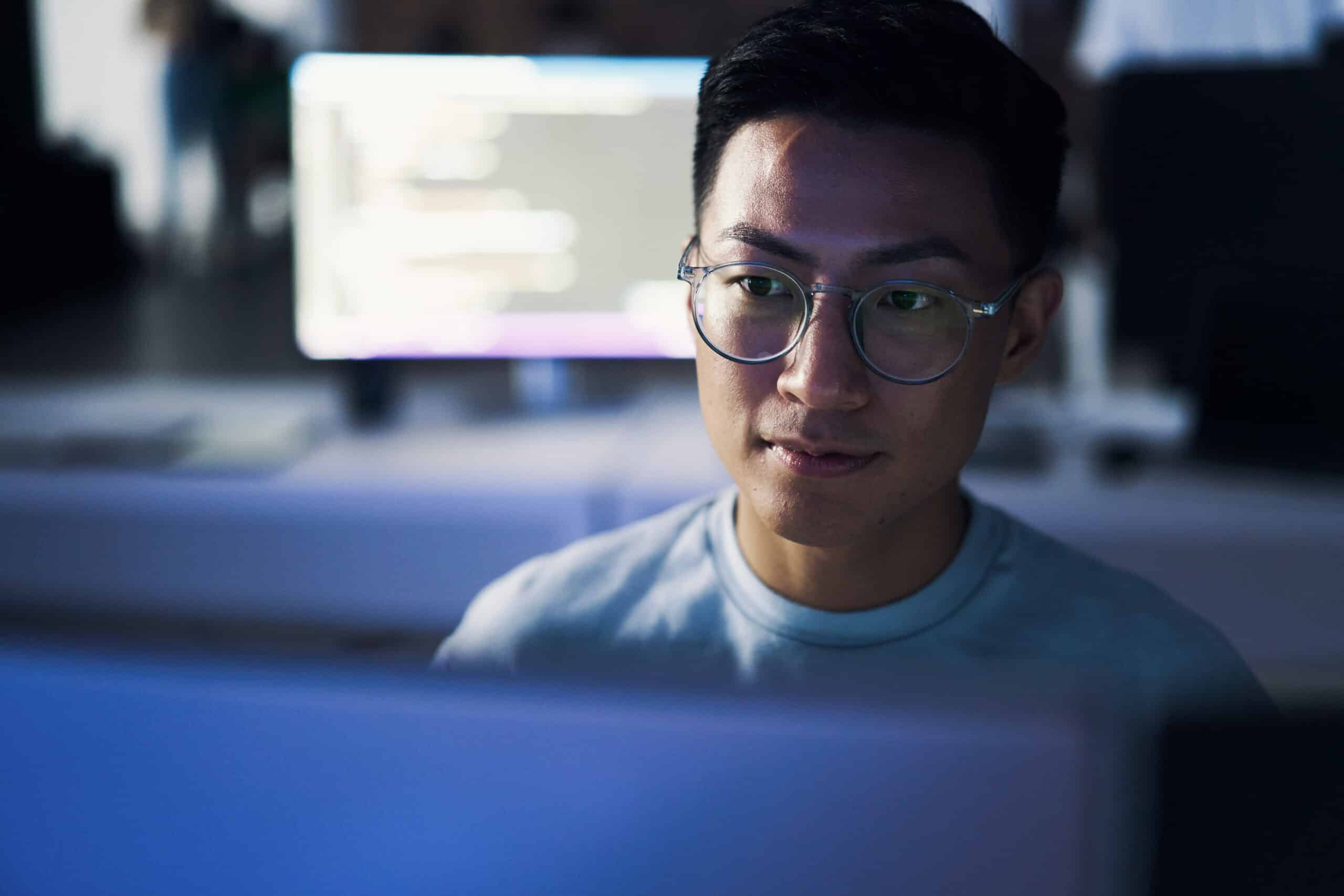 Man with glasses works at a computer, coding for a location intelligence consulting project.