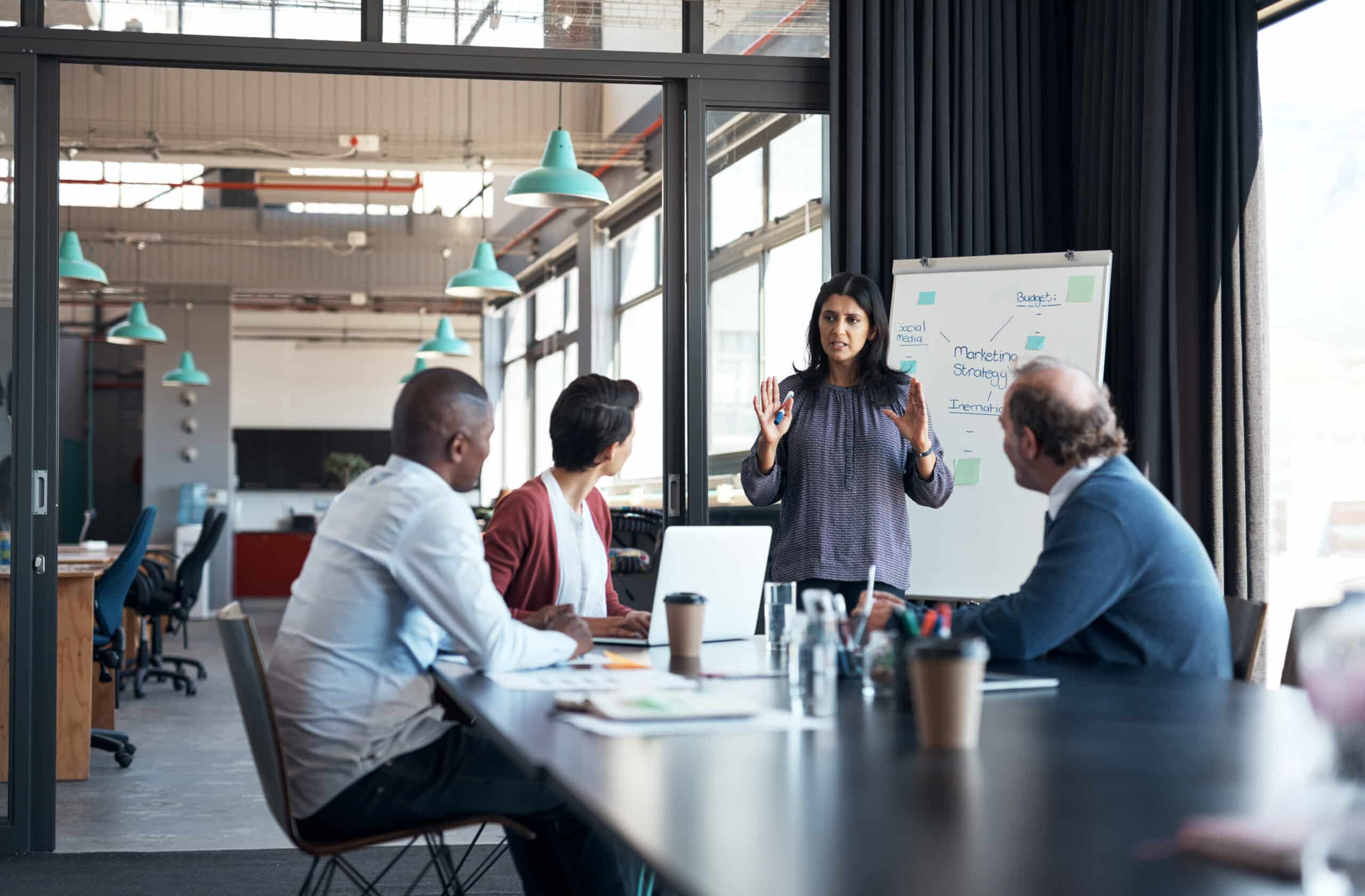 A woman presents to three colleagues in a modern office, discussing location intelligence consulting.