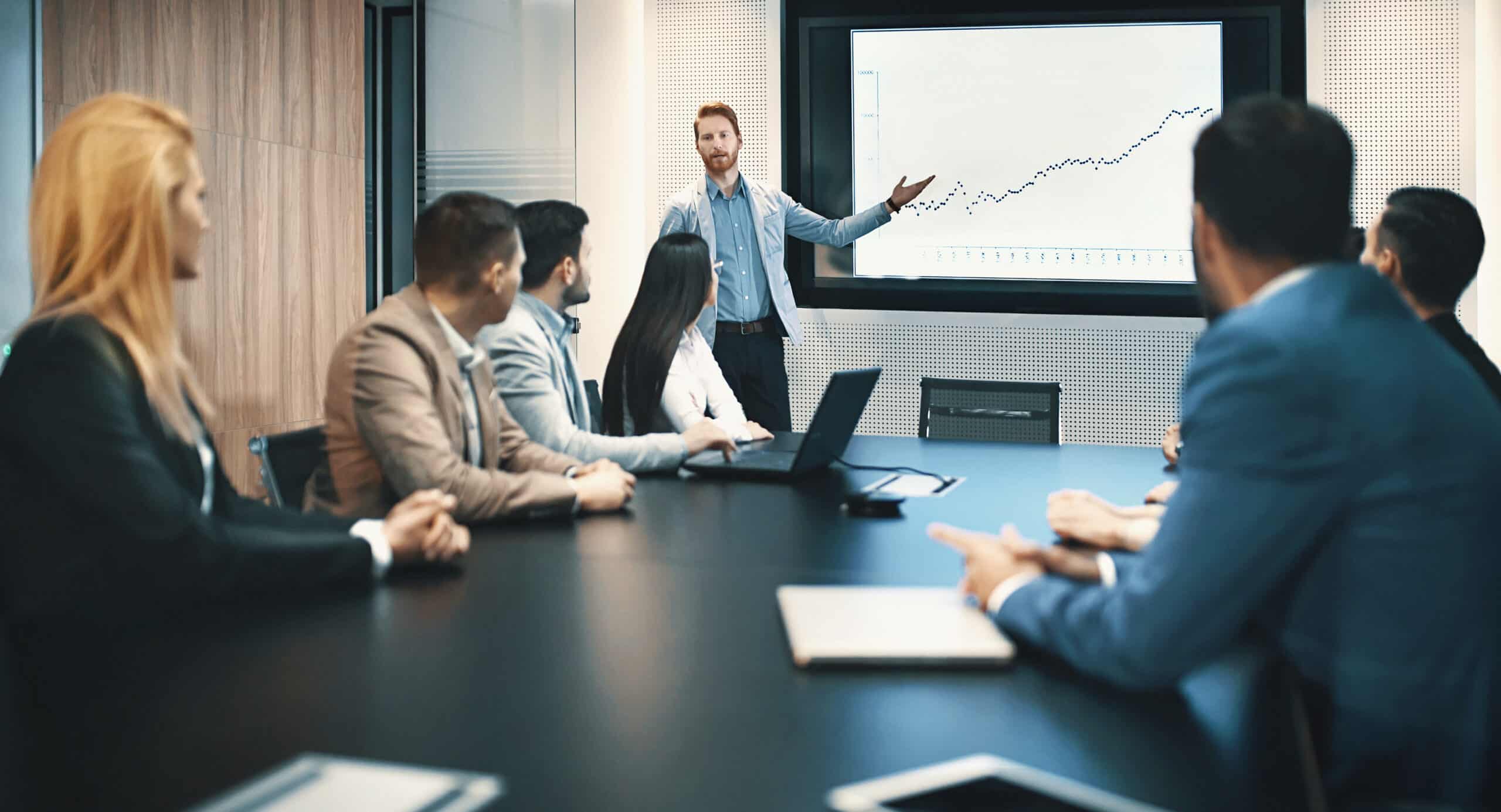 Man presenting a rising line graph on natural language processing (NLP) to colleagues in a conference room.