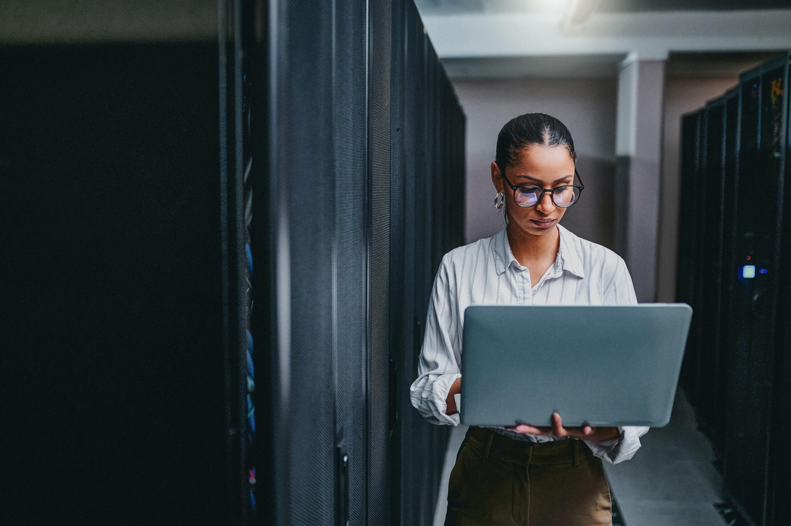 Woman using a laptop in a server room, working on natural language processing (NLP) projects.