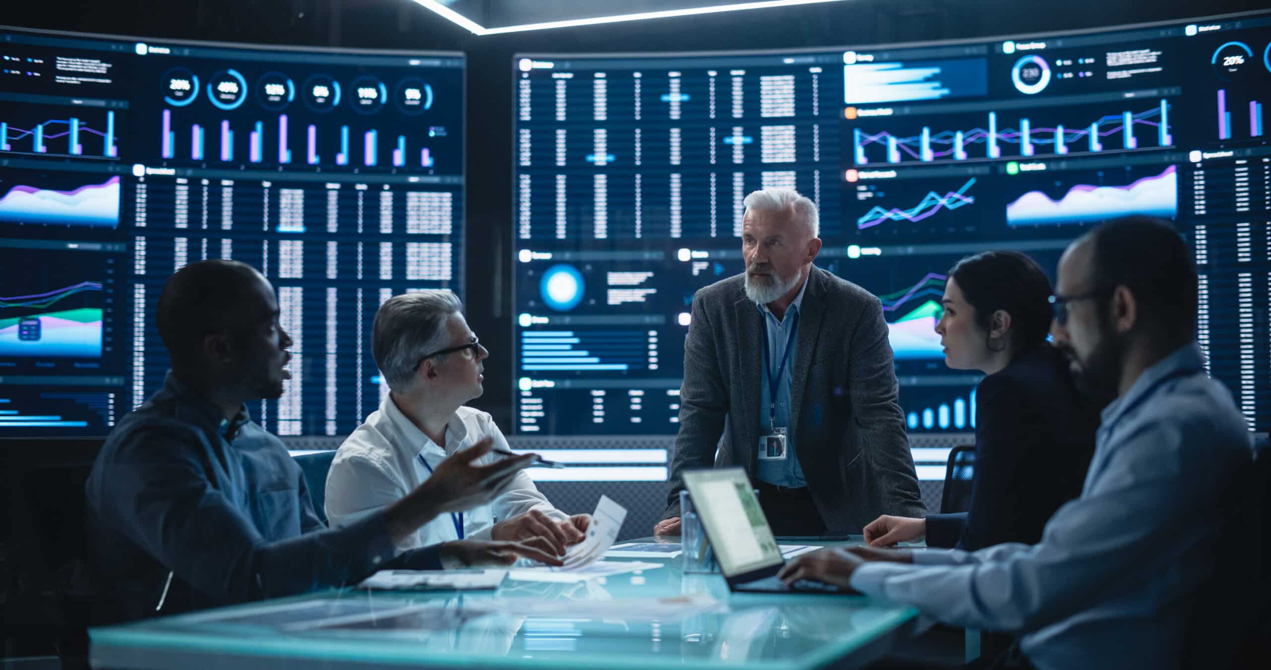 Five people discuss data as predictive maintenance consulting charts and graphs display behind them.