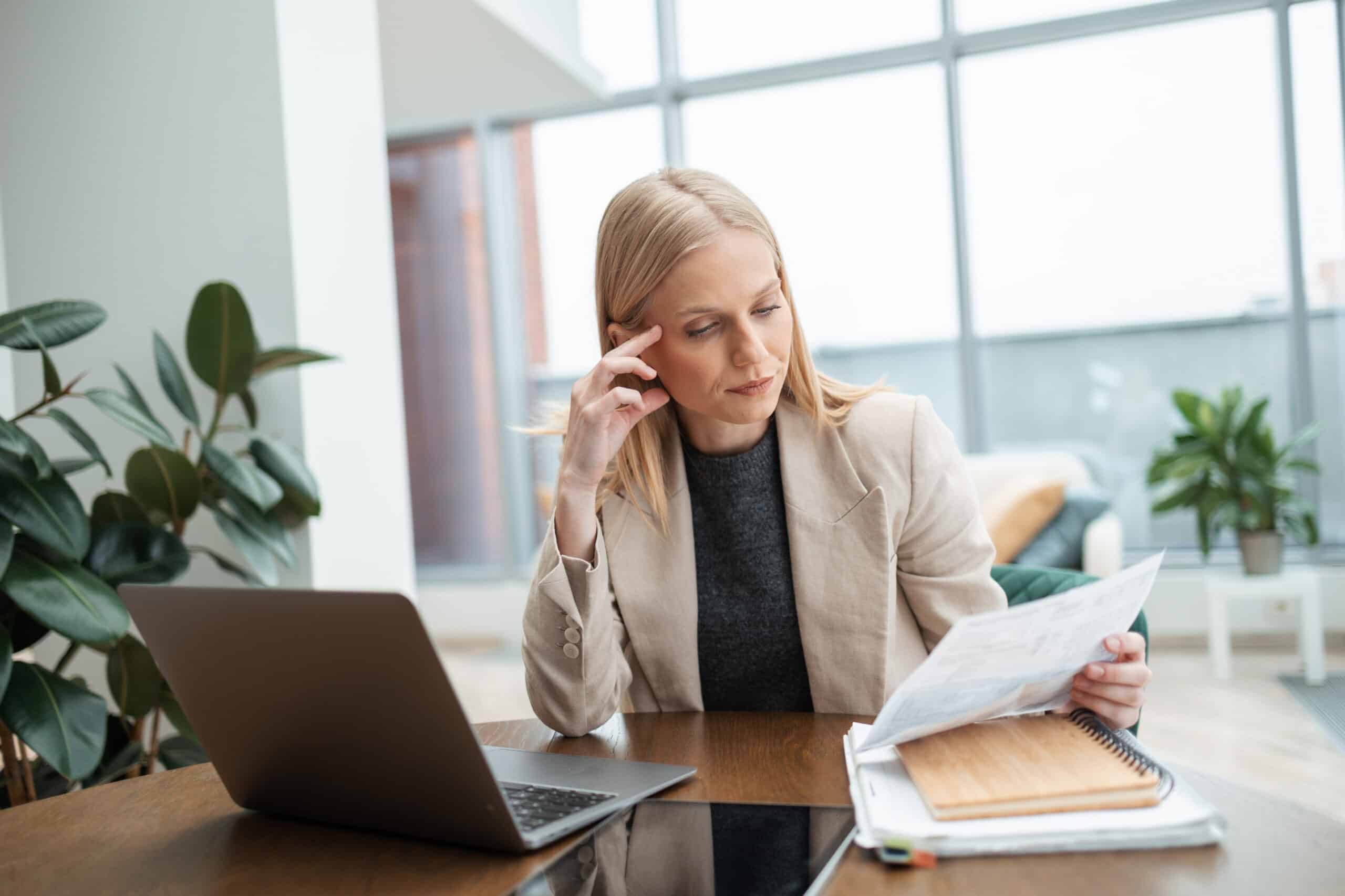 Woman at desk with laptop reviewing predictive maintenance consulting documents in modern office.
