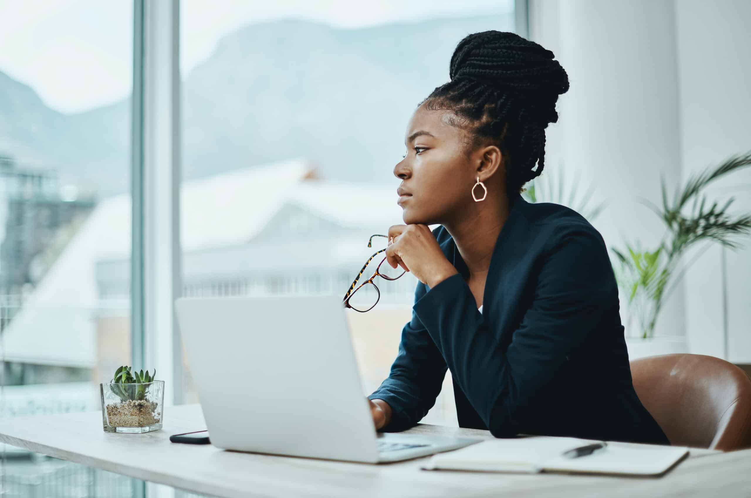 Woman in a blazer sits at her desk, reflecting on predictive maintenance consulting solutions.