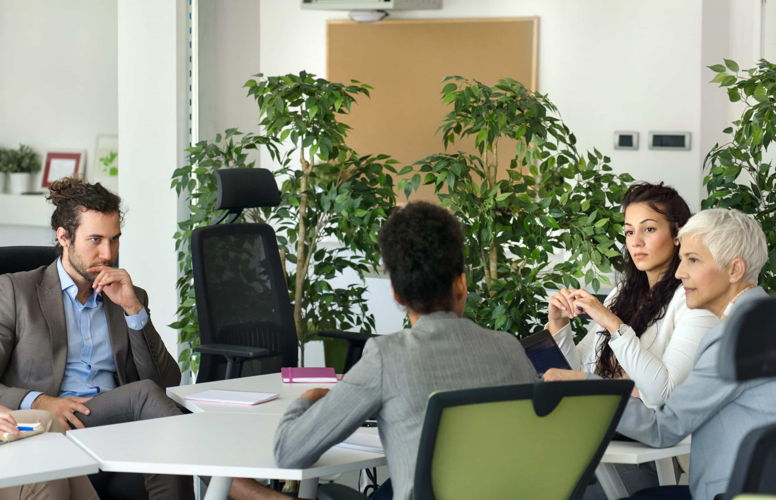 Four people discuss real estate fair market value analysis in a modern office with plants.