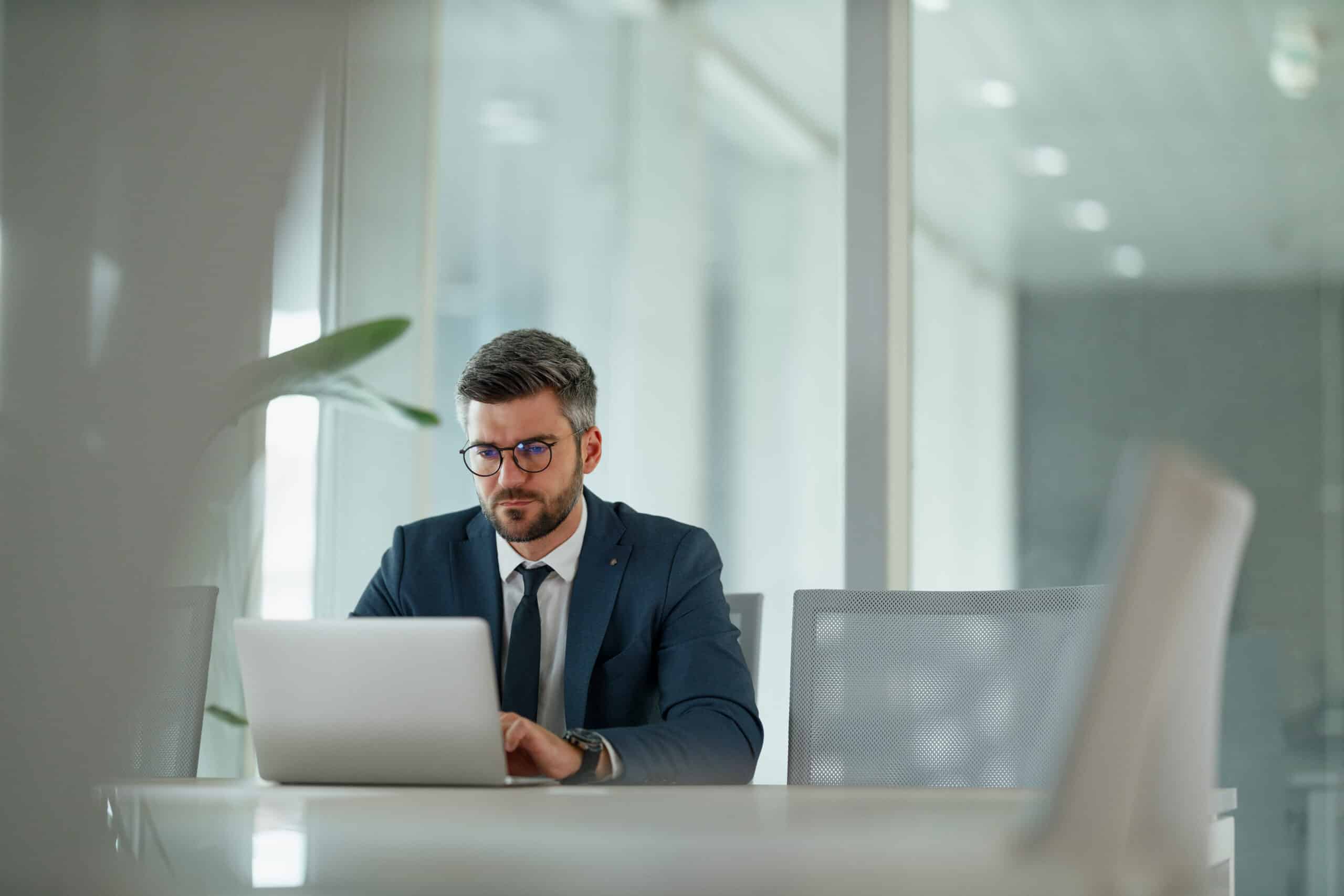 Man in suit working on laptop at desk, focused on real estate fair market value analysis.