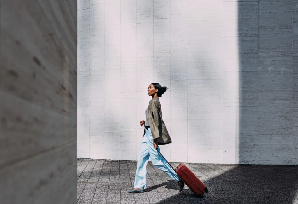 Confident woman walking with red suitcase against a modern urban wall. Ideal for travel, business, and lifestyle concepts.