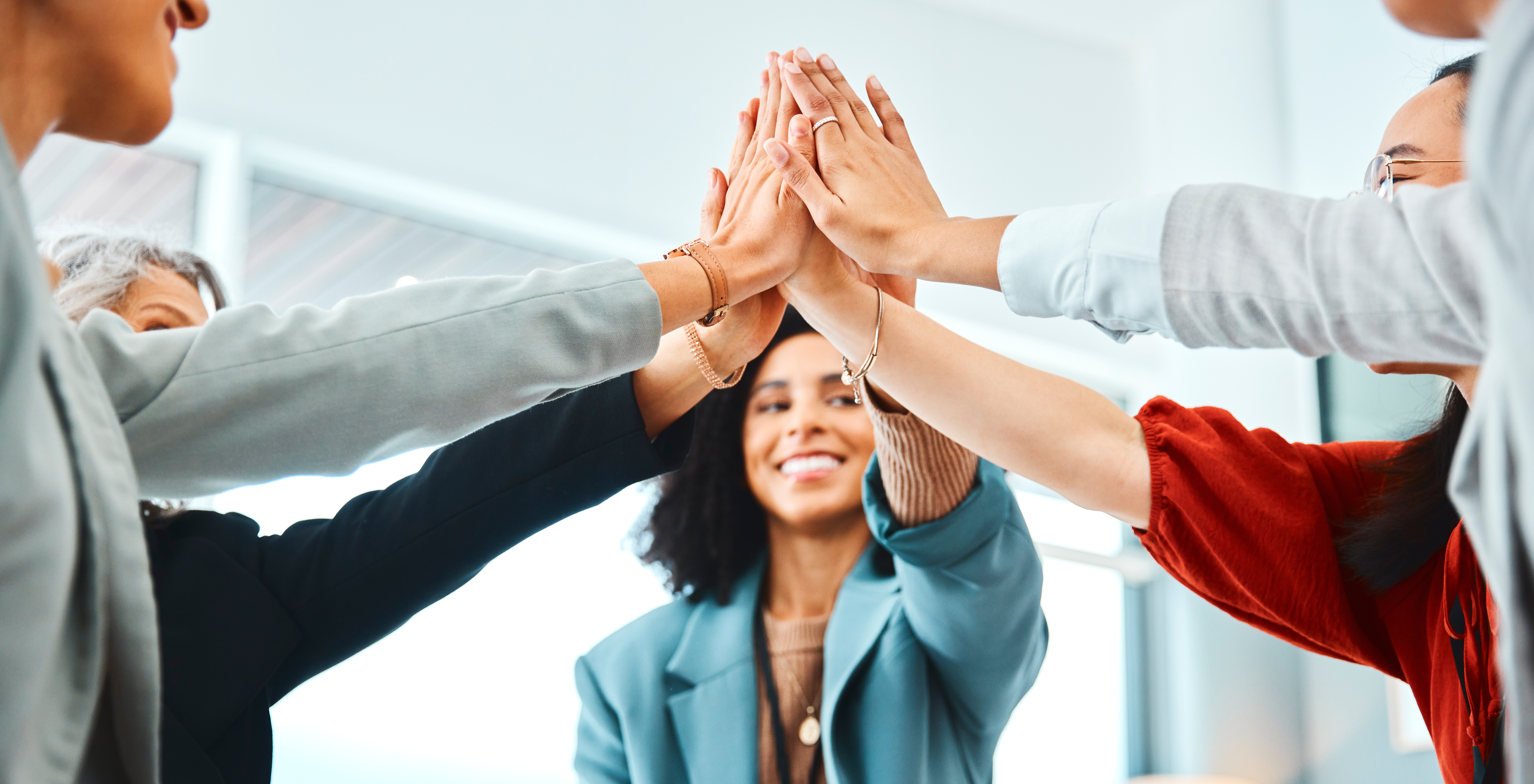 Five Proptech Consultants smiling and joining hands in a high-five gesture in an office setting.