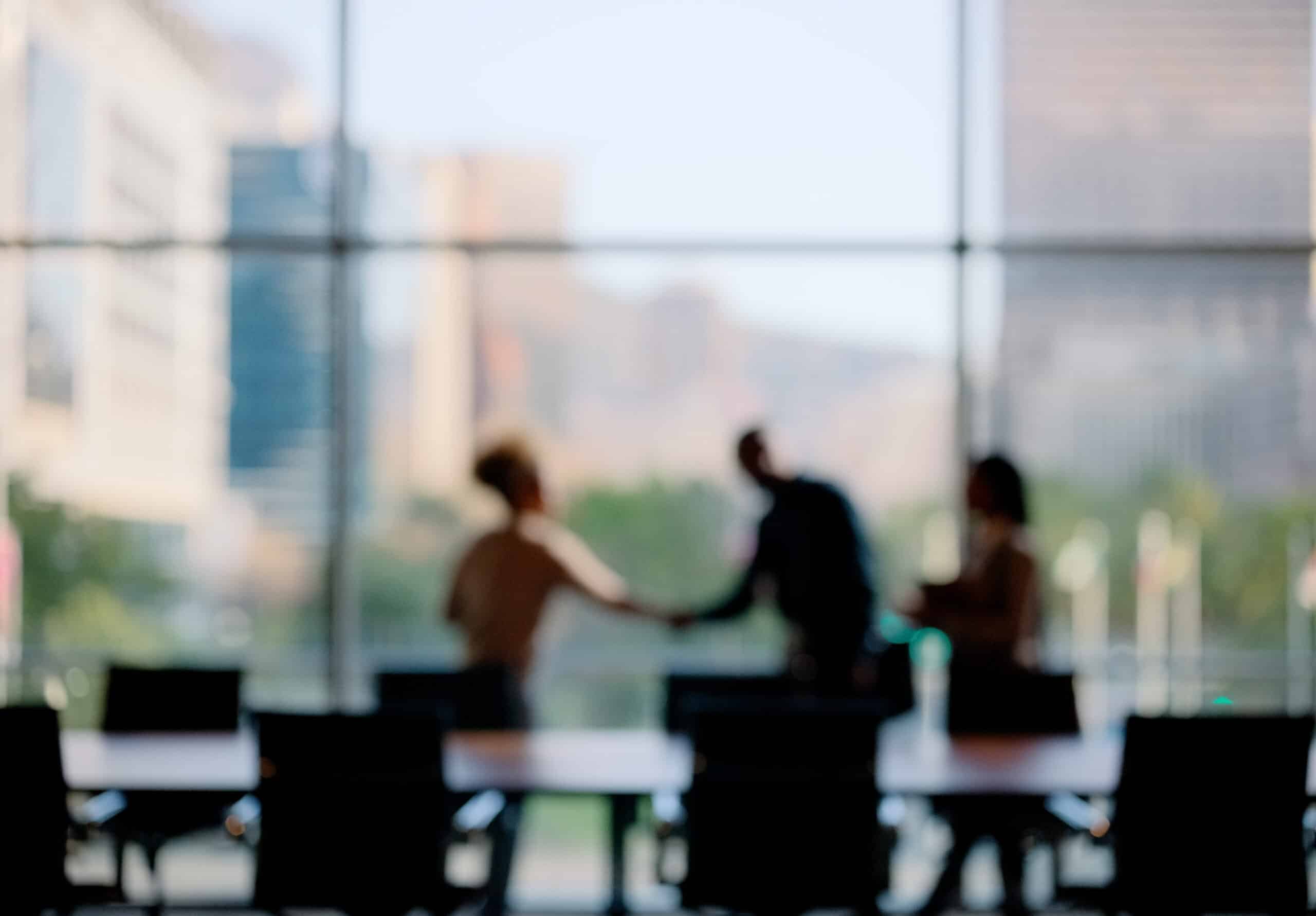 Blurred image of three people shaking hands—Enterprise Systems Transformation in a modern office.
