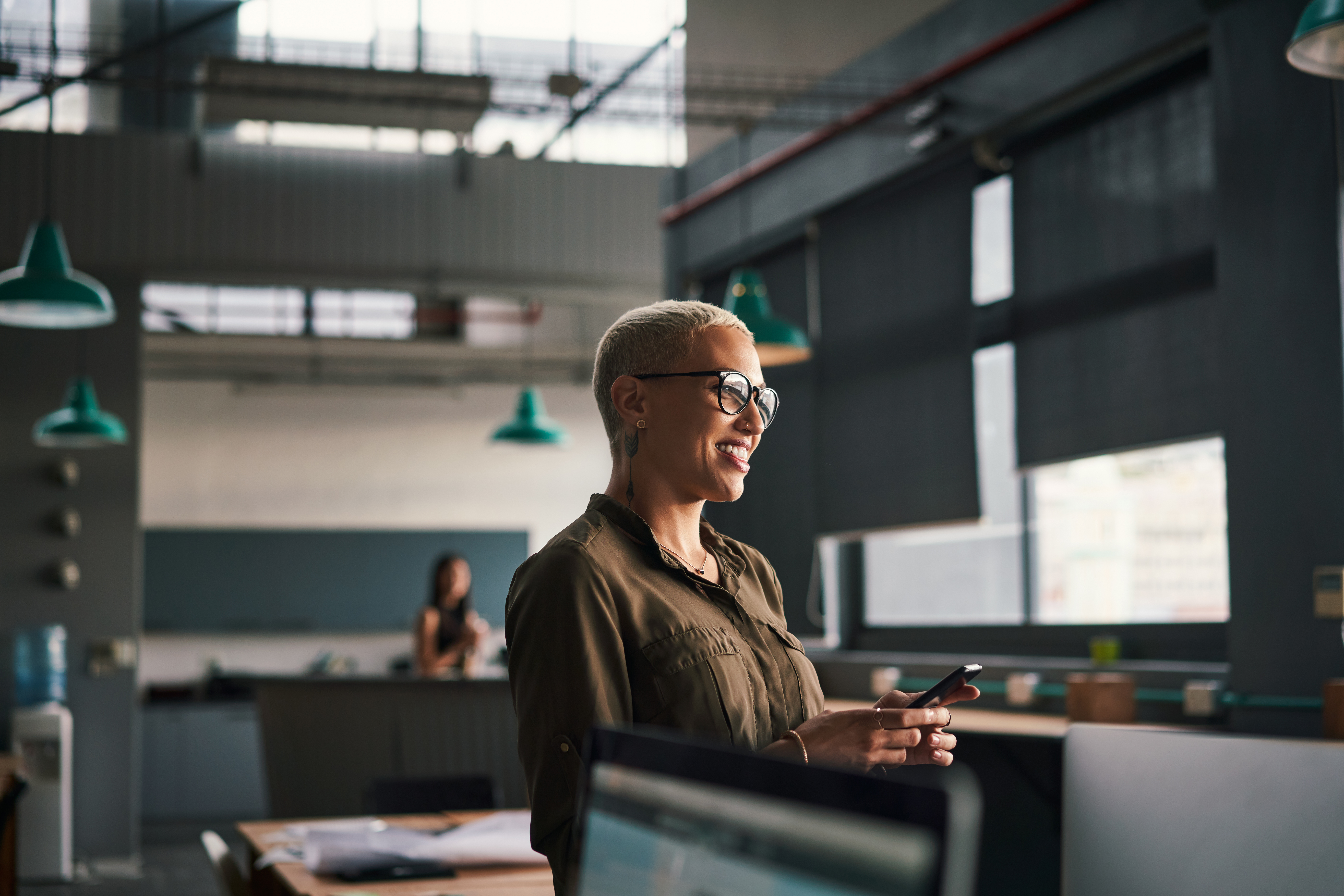 Smiling person with glasses holding a phone in a modern office, focused on CRE Due Diligence.