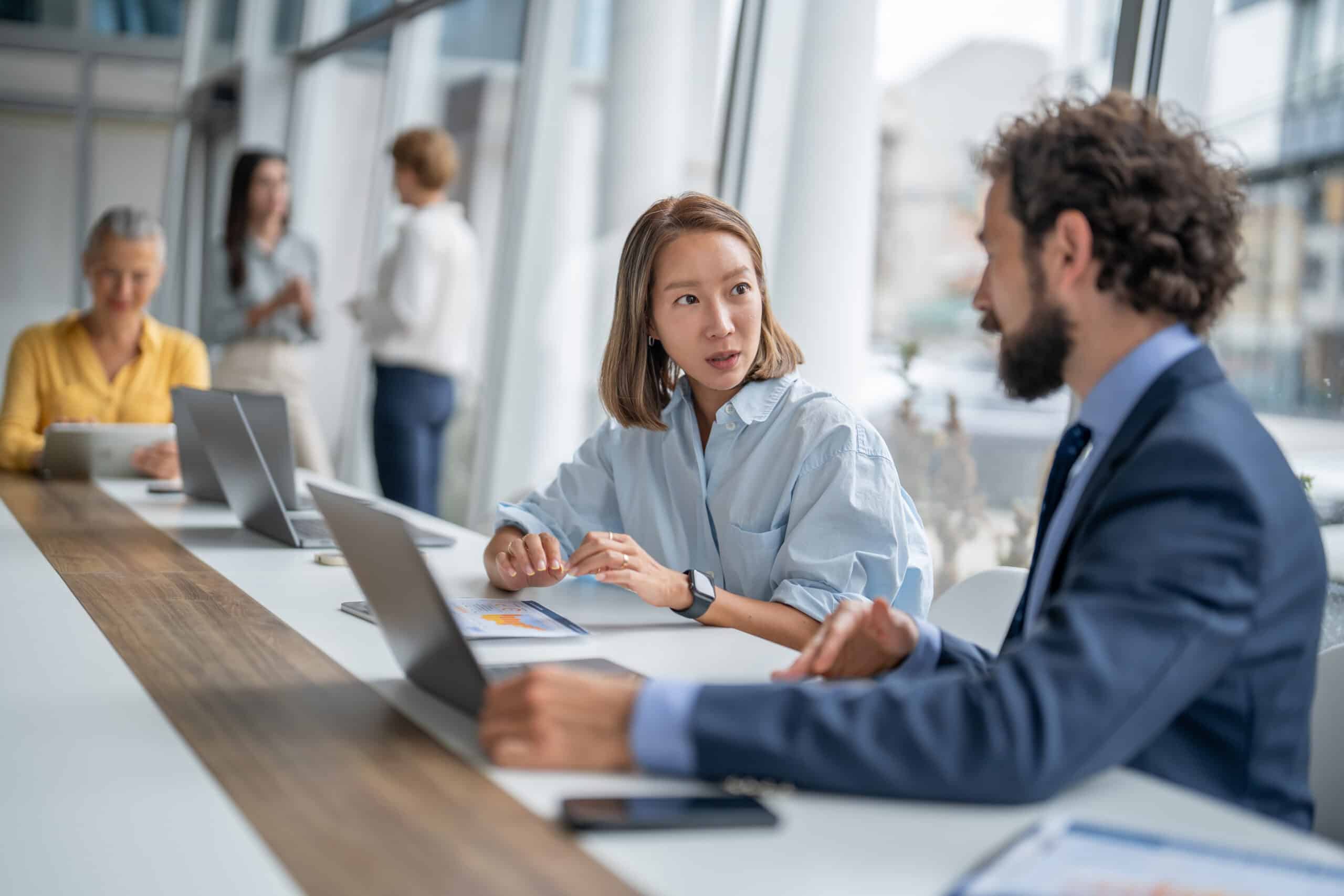 Two colleagues, including AI consultants, discuss work at a conference table in a modern office.