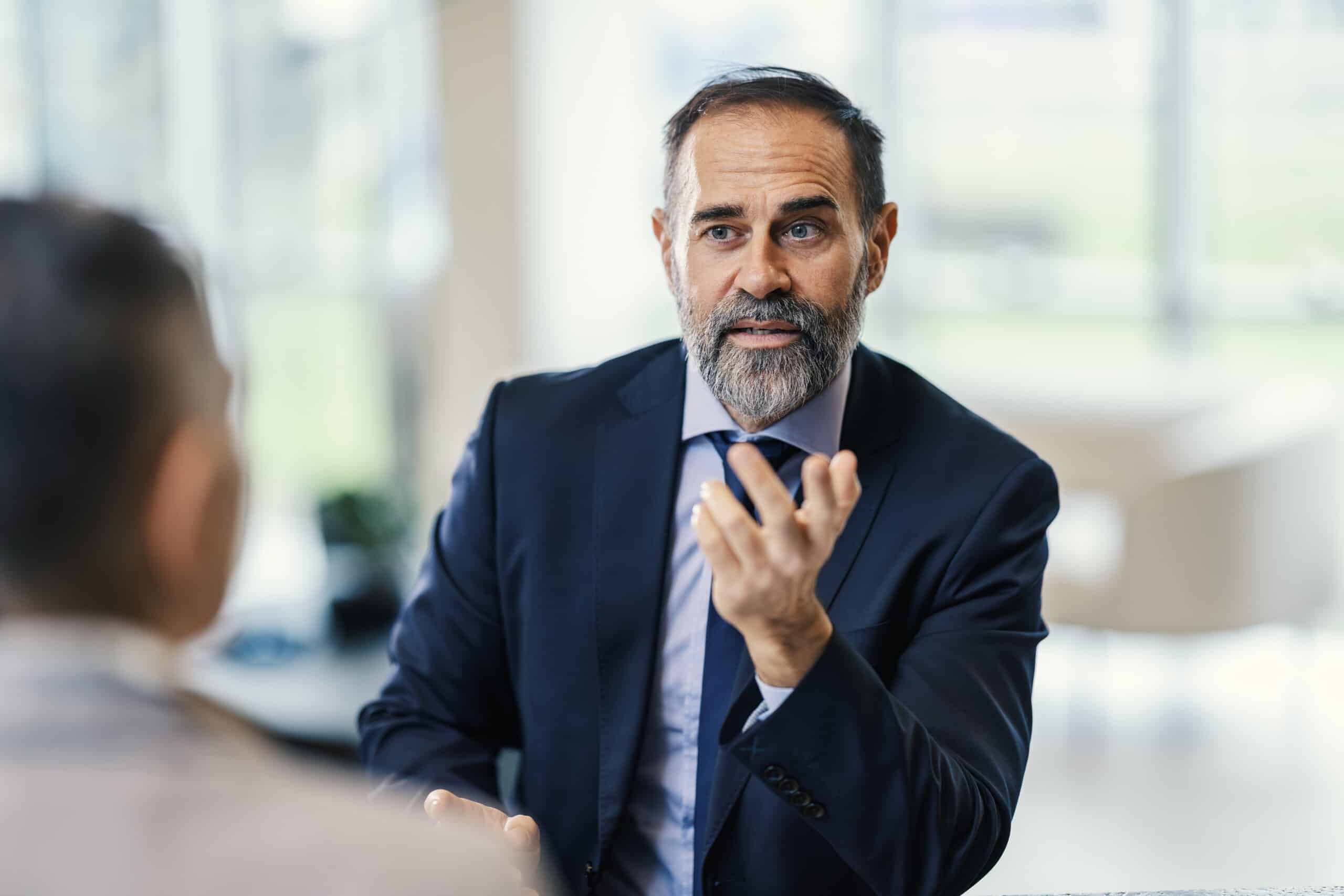 Bearded man in suit discusses CRE Tax Management with colleague in an office setting.