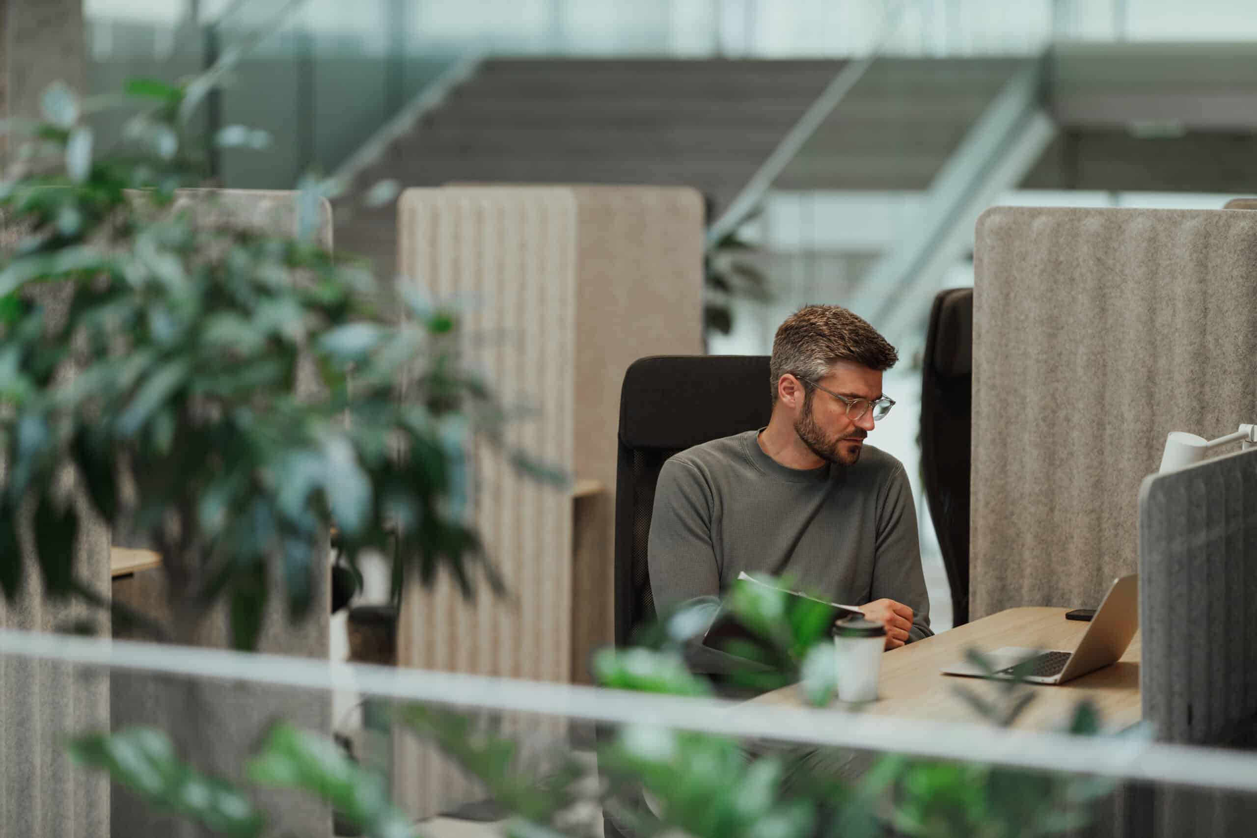 Man working on a laptop in a CRE Change Management-focused office with plants and partitioned desks.