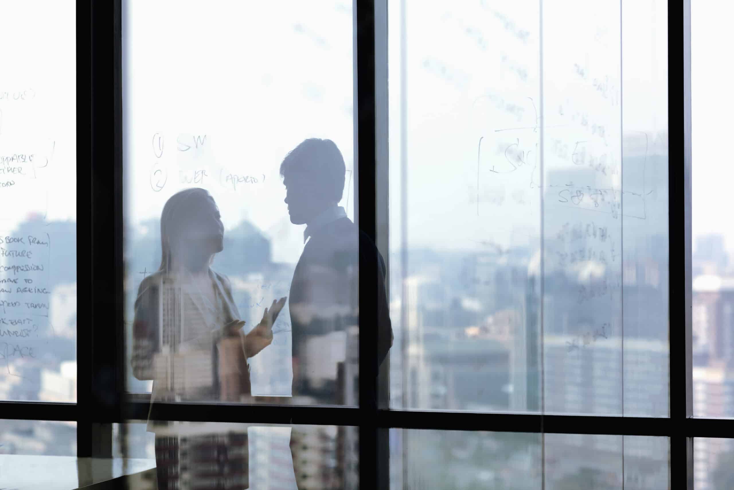 Two people discuss CRE Risk Management, silhouetted before a city skyline window.