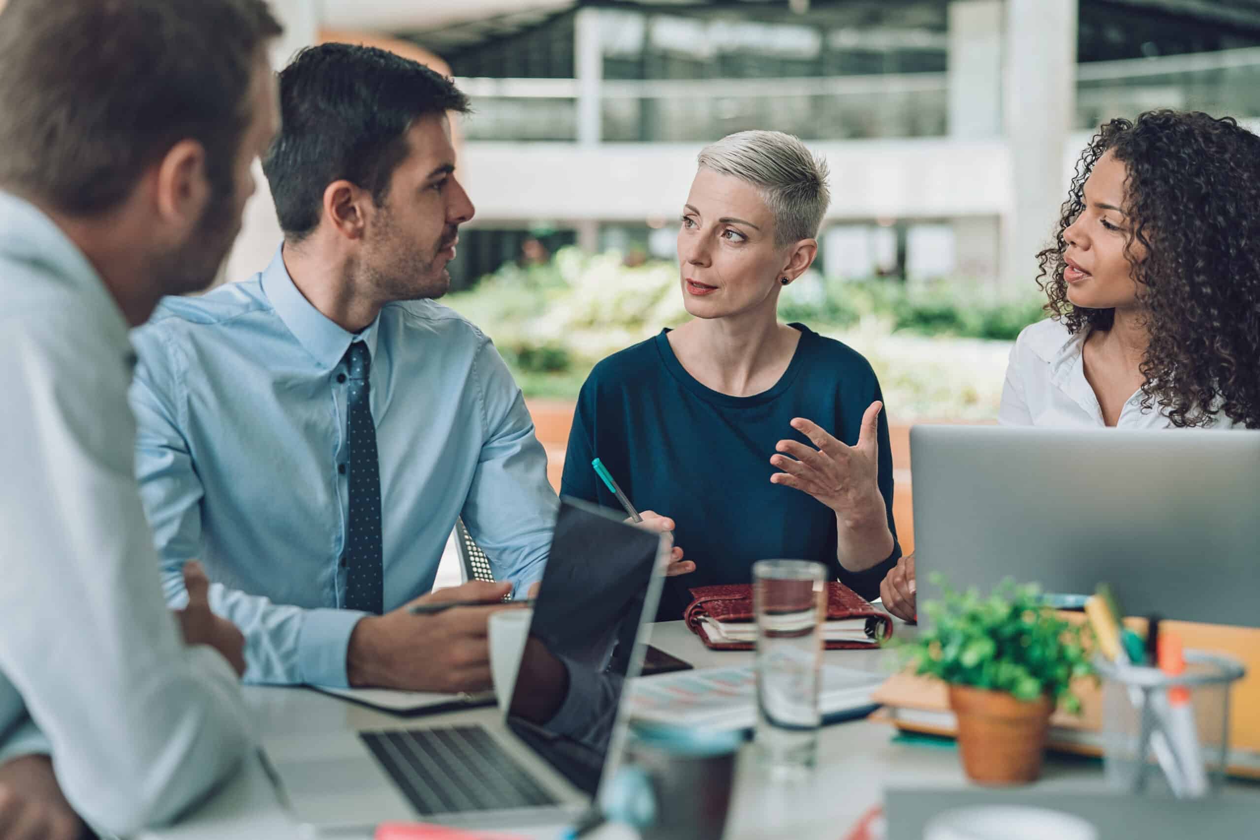 Four colleagues discuss IT Governance around a table with laptops and documents.