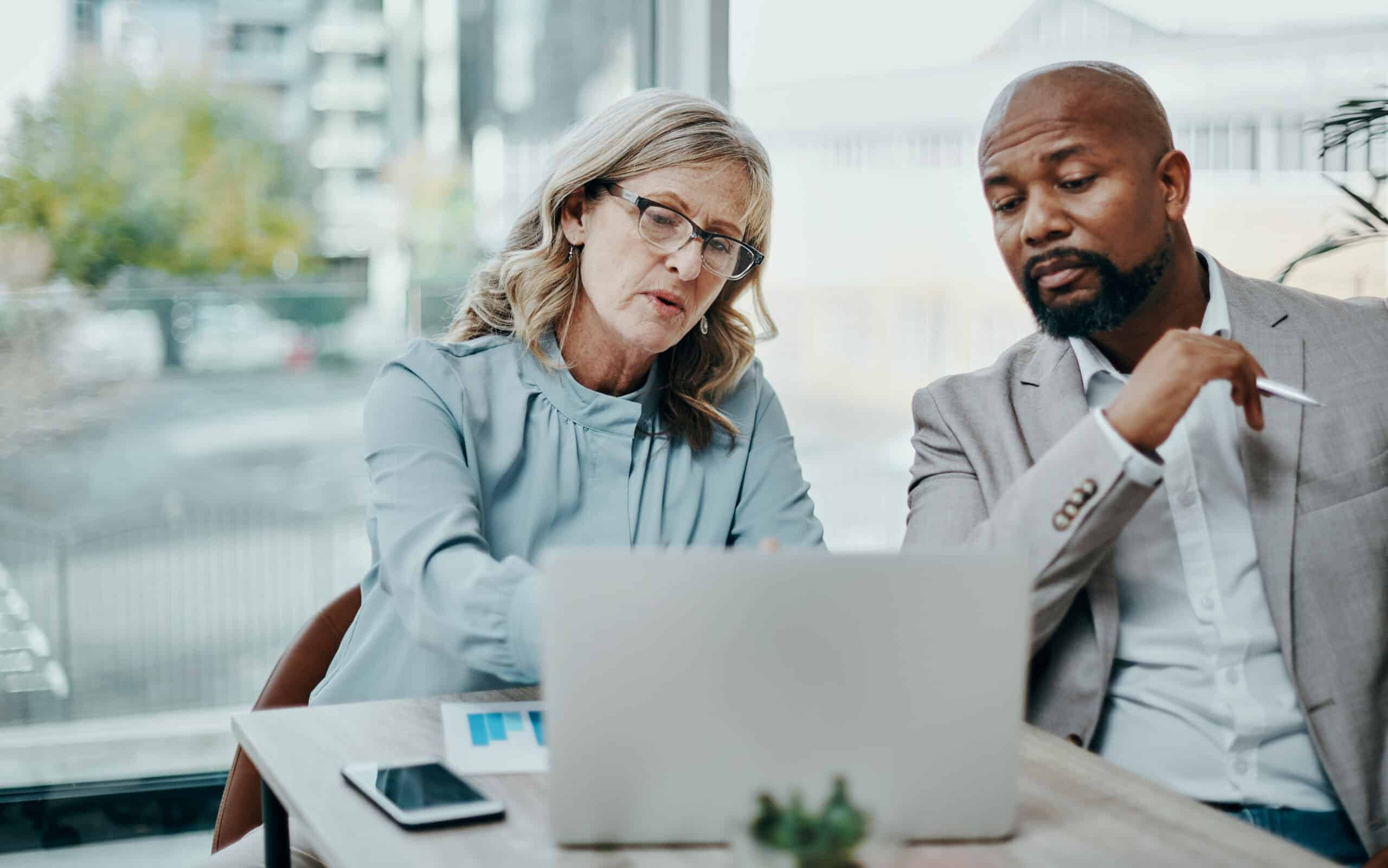 Two colleagues discuss CRE Transaction Management while looking at a laptop in a modern office.