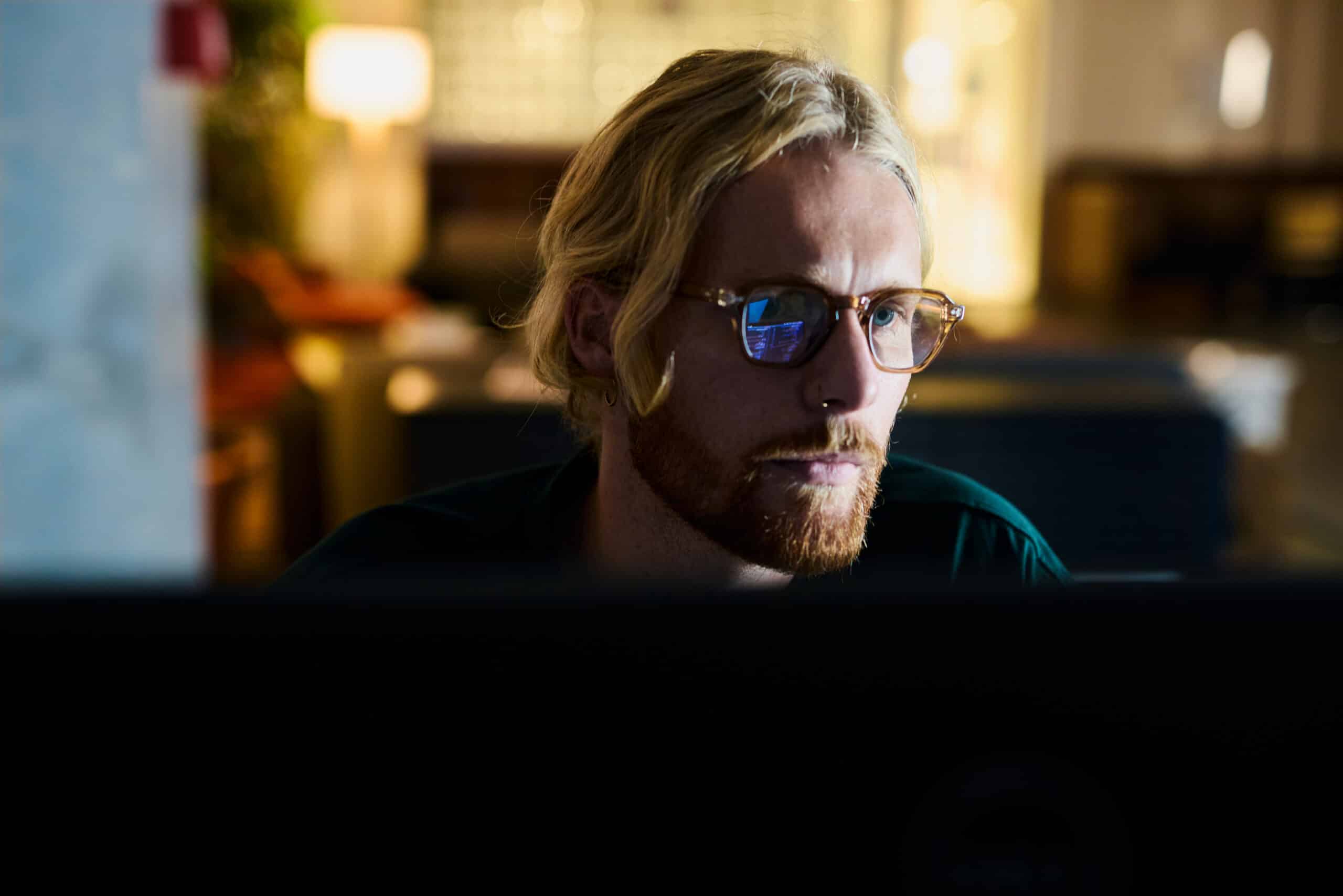 Person with glasses and blond hair working on Smart Building Consulting in a dimly lit room.