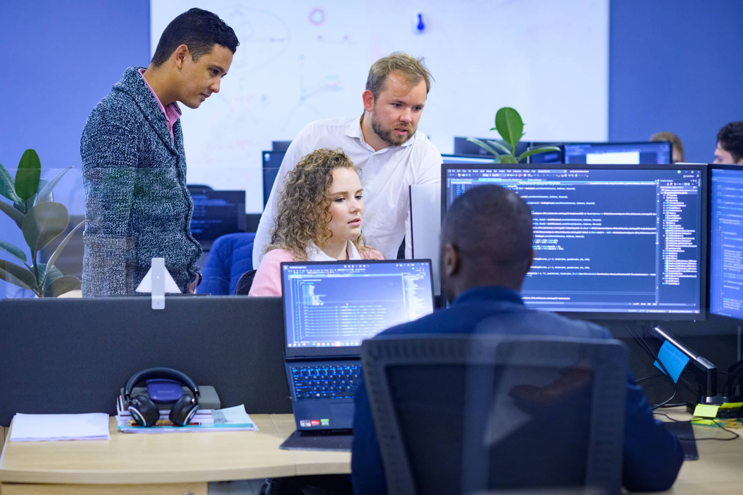 Four people collaborate at desks on Digital Twins in a modern, code-driven office workspace.
